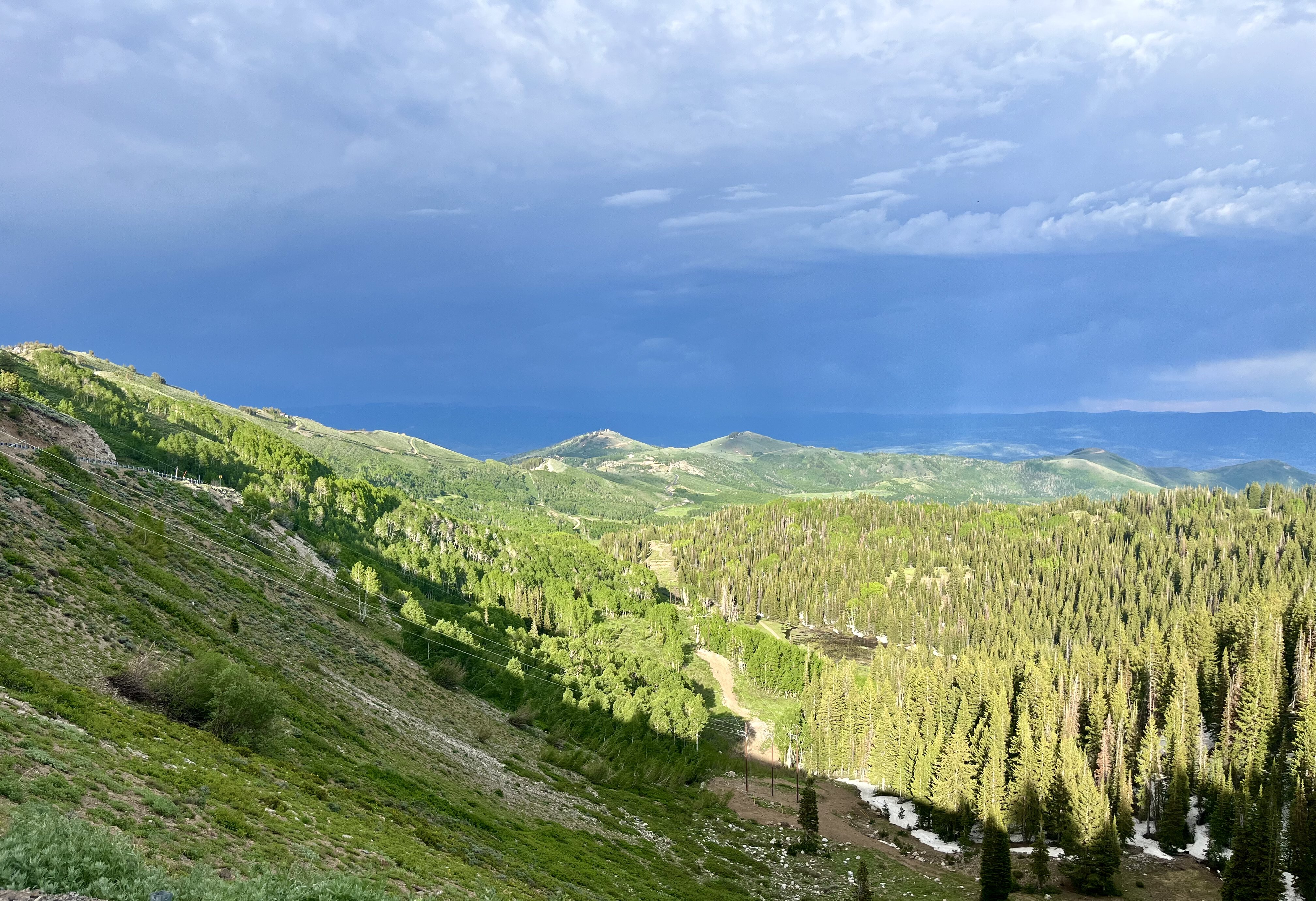 Mountain pass view with green trees, mountain peaks and distant stormy clouds. 