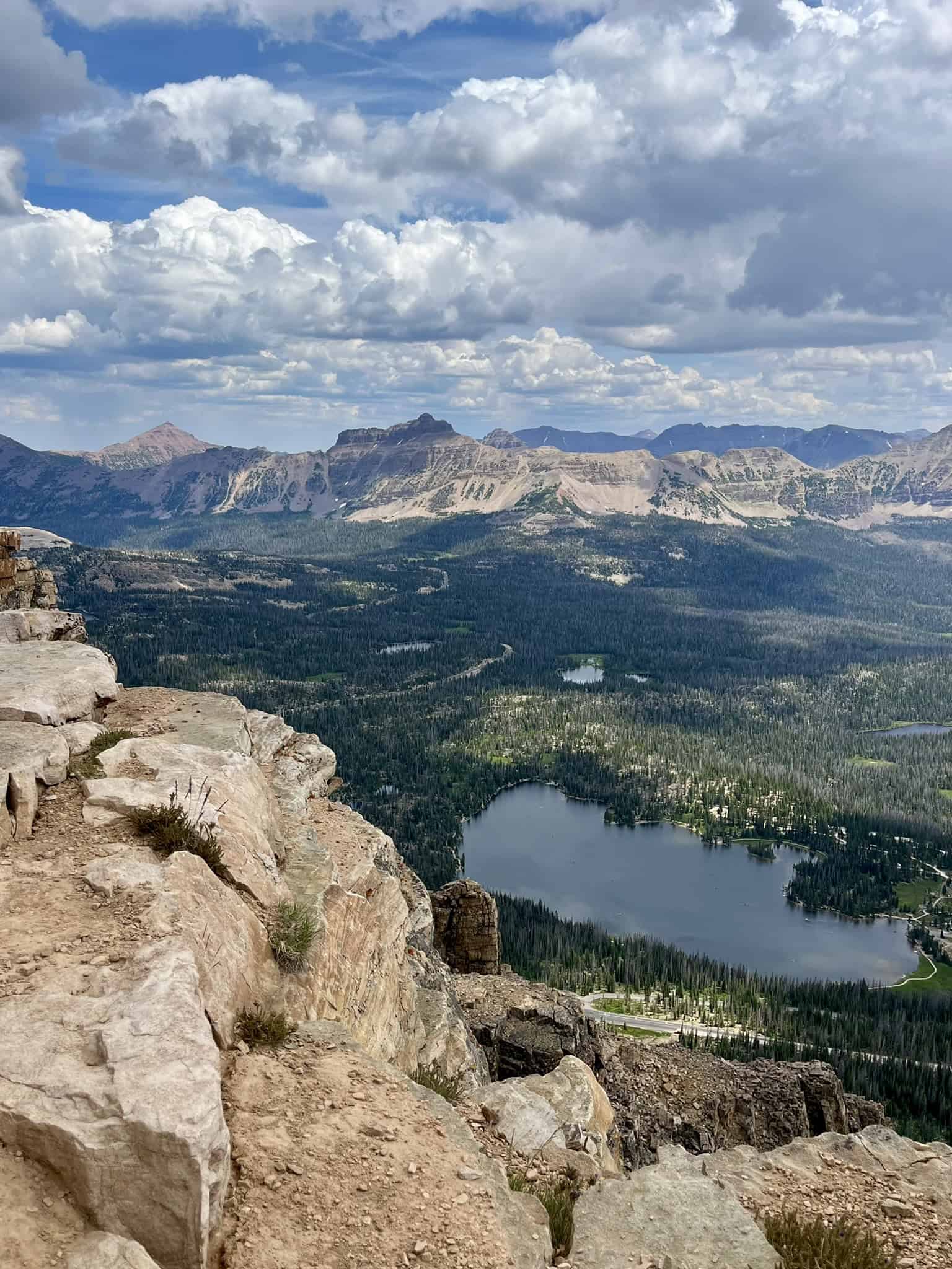 Dramatic mountain landscape from a rocky mountain peak, with a big blue lake in the right corner, and mostly cloudy skies. 