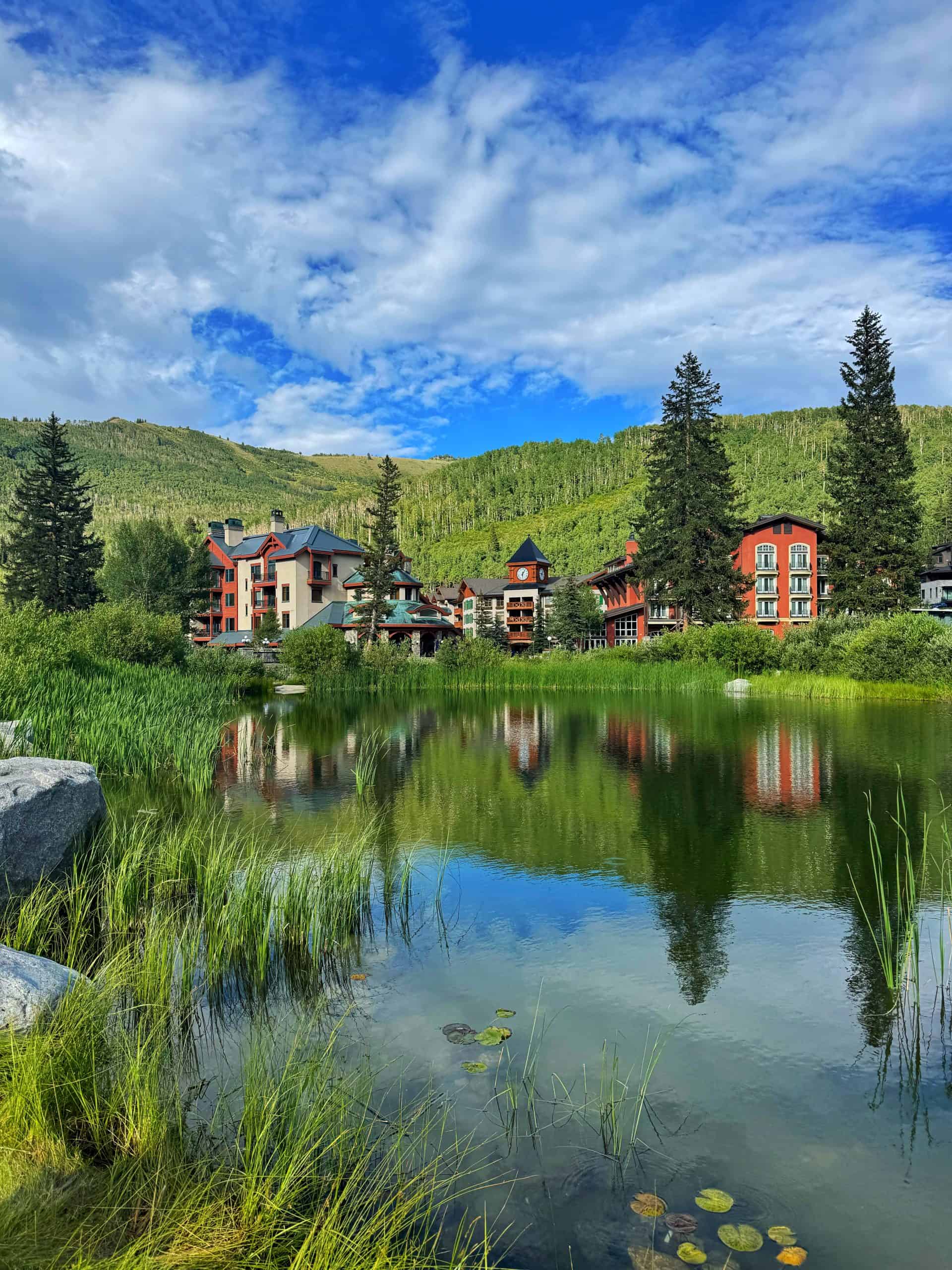 Solitude Mountain Village reflected in a pond, surrounded by green hills and summer scenery.