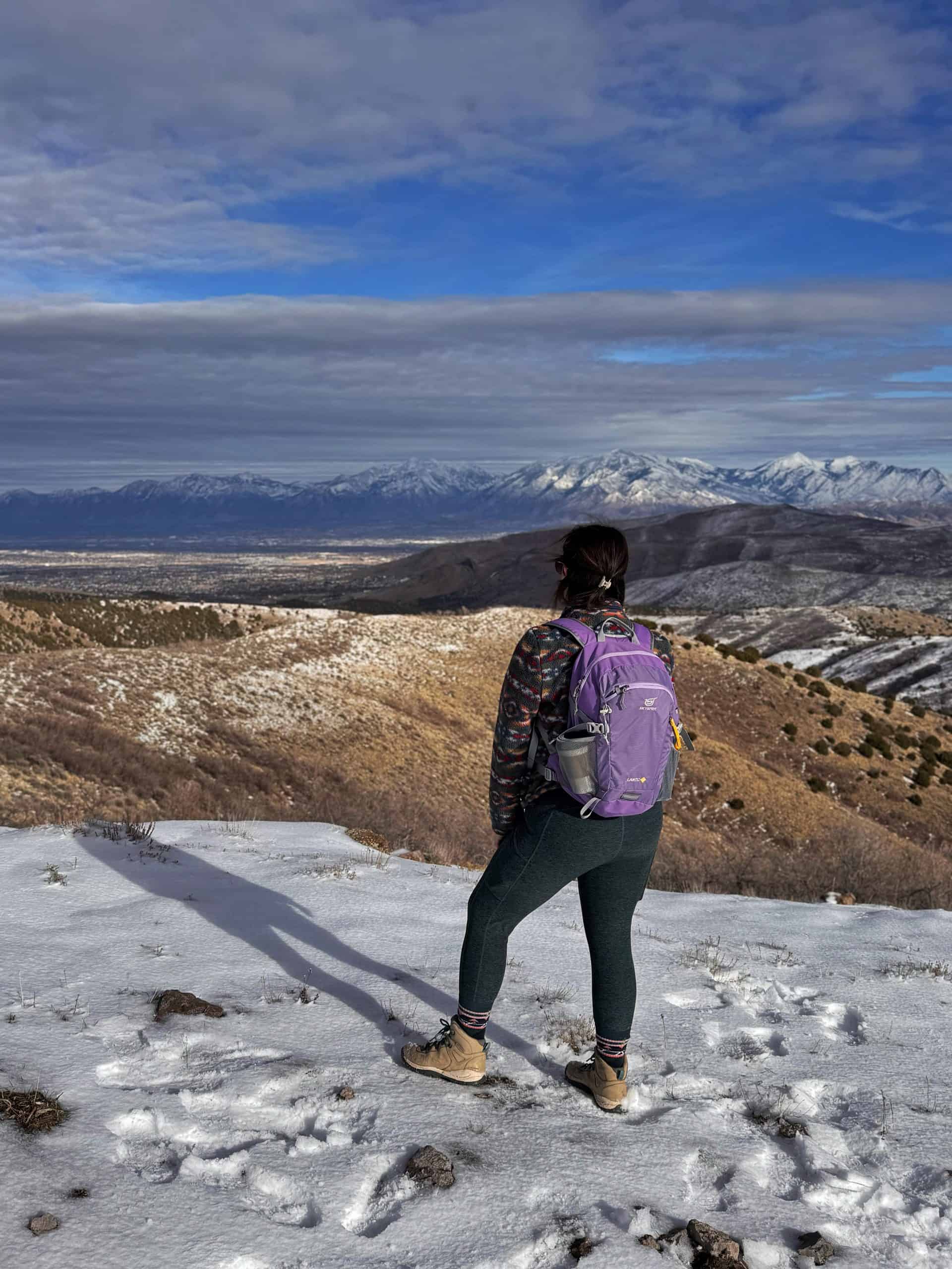 Pretty girl with purple backpack gazing at wide open mountain vista, with lingering snow. 