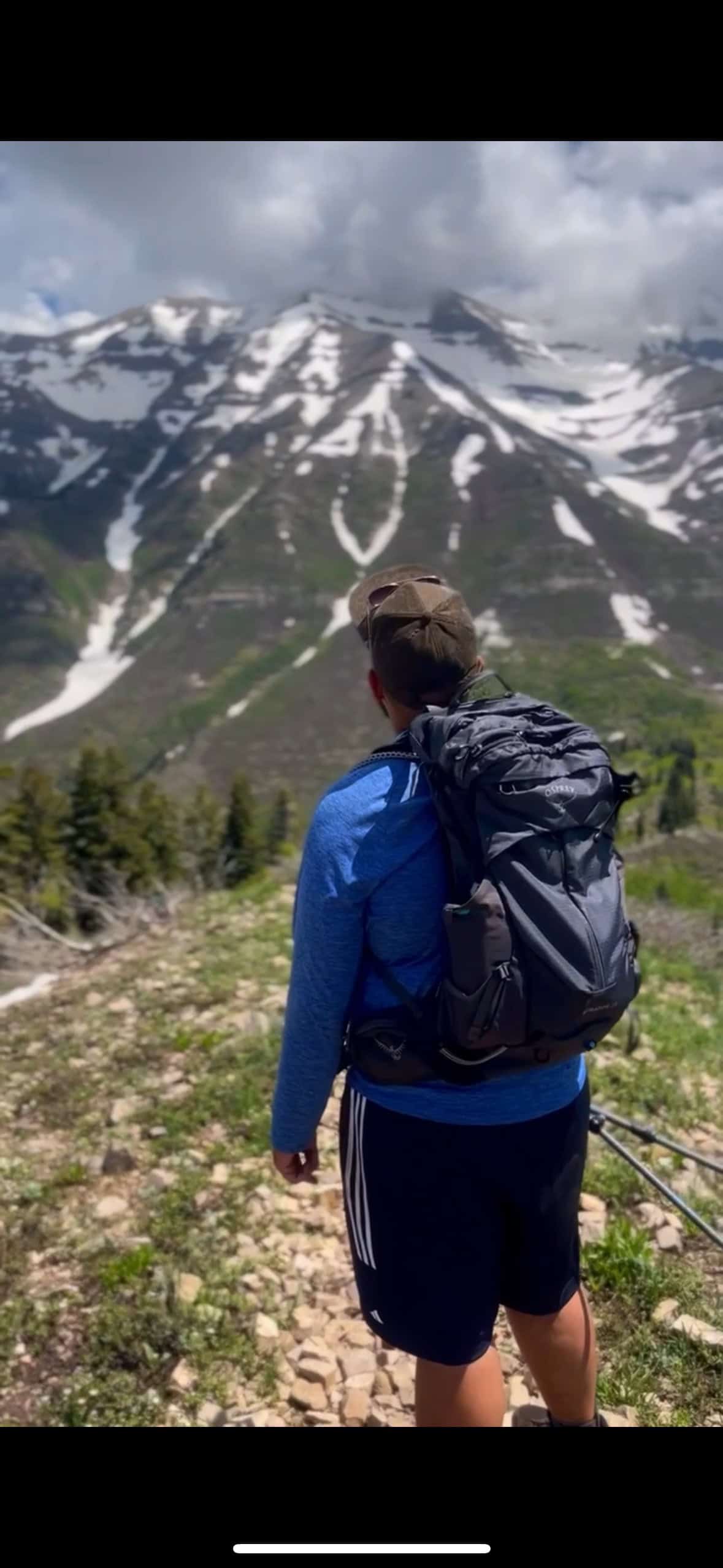 A hiker walks along a sunlit trail carrying a fitted Osprey daypack