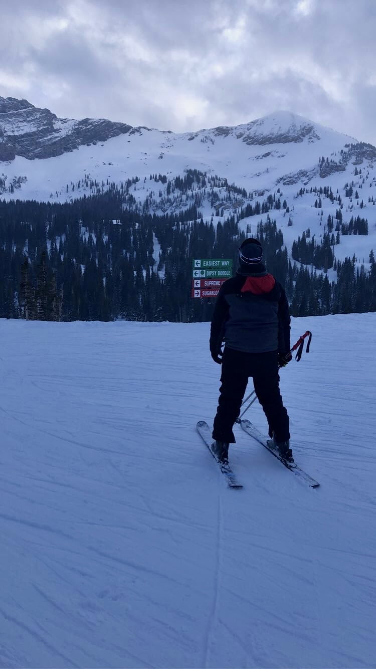 A skier standing on a snowy slope at Alta Ski Resort with rugged mountains in the background.