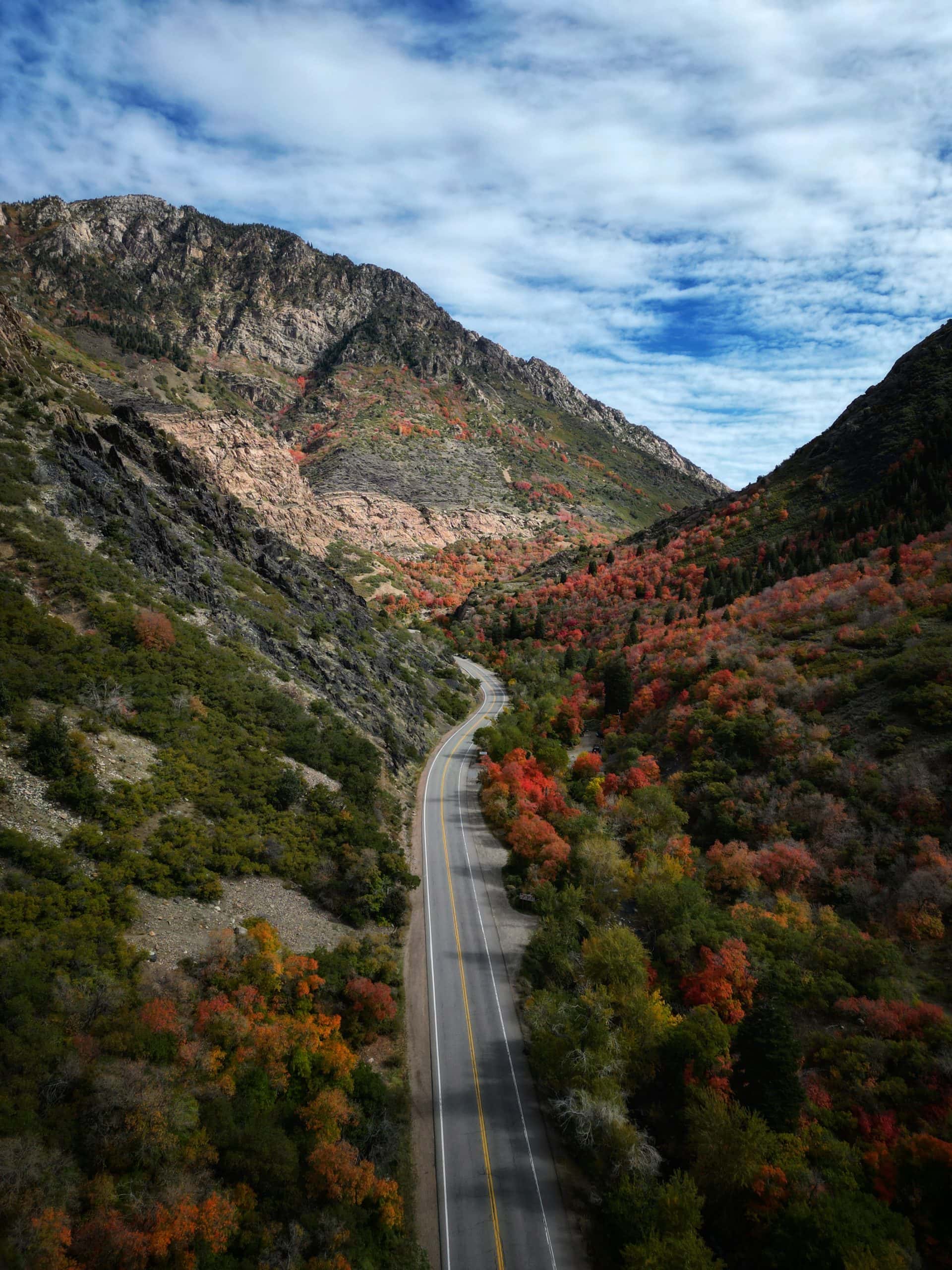A curved road running through Big Cottonwood Canyon with colorful autumn foliage on steep mountainsides.