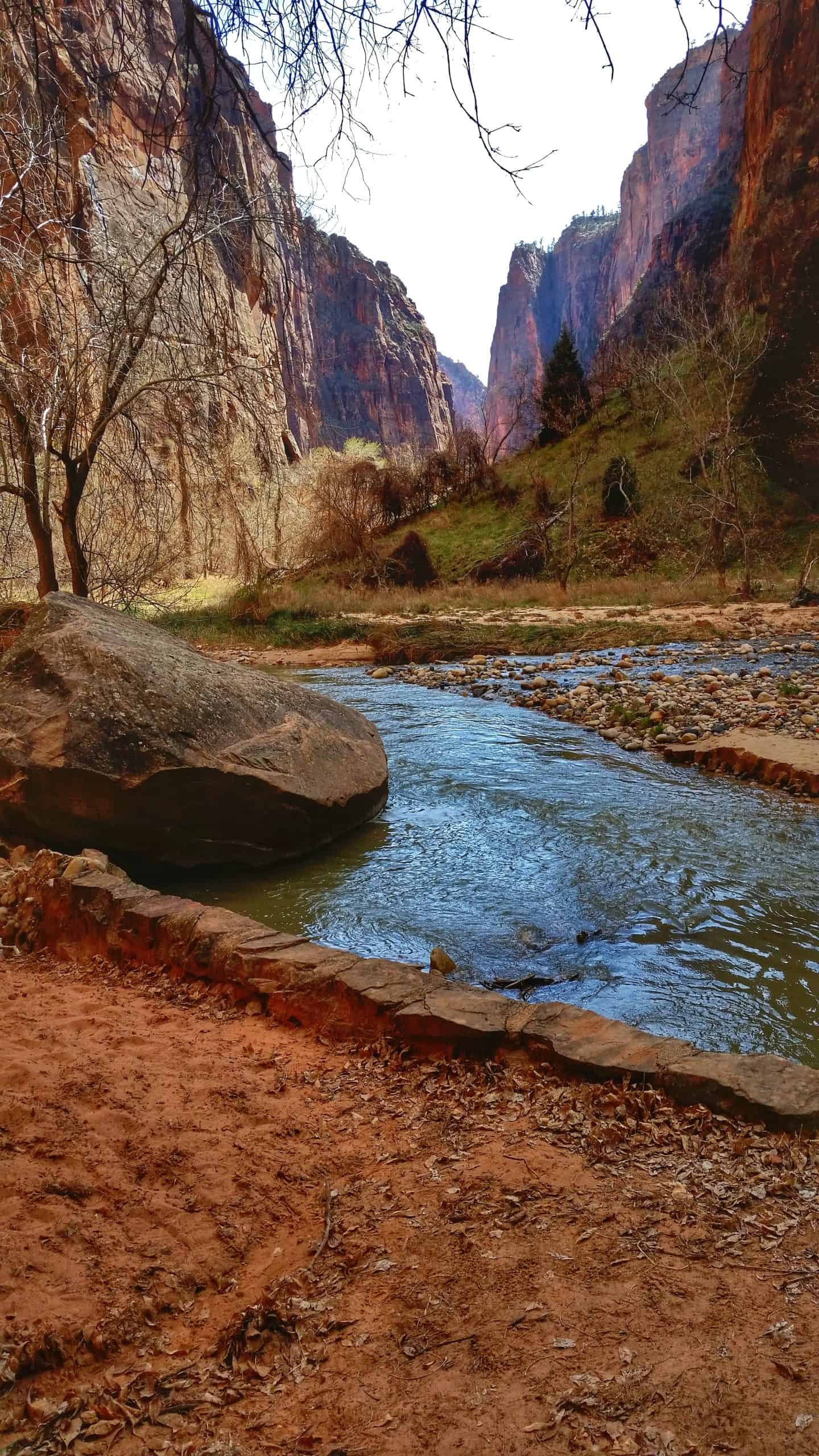 A gentle river flowing in the foreground, with narrow canyon walls in the distance