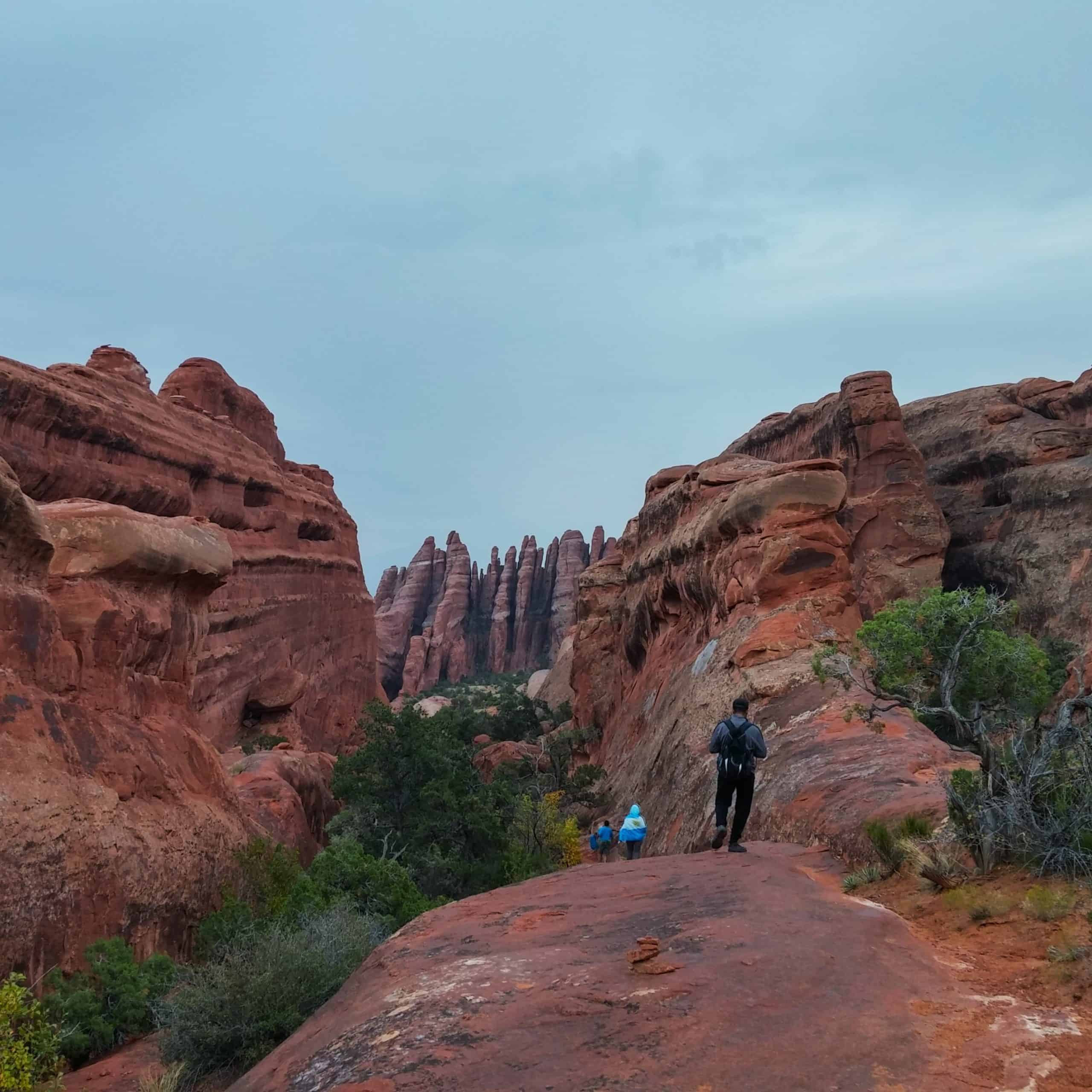 Hikers walking along the Devils Garden Loop surrounded by towering red rock formations in Arches National Park, Utah
