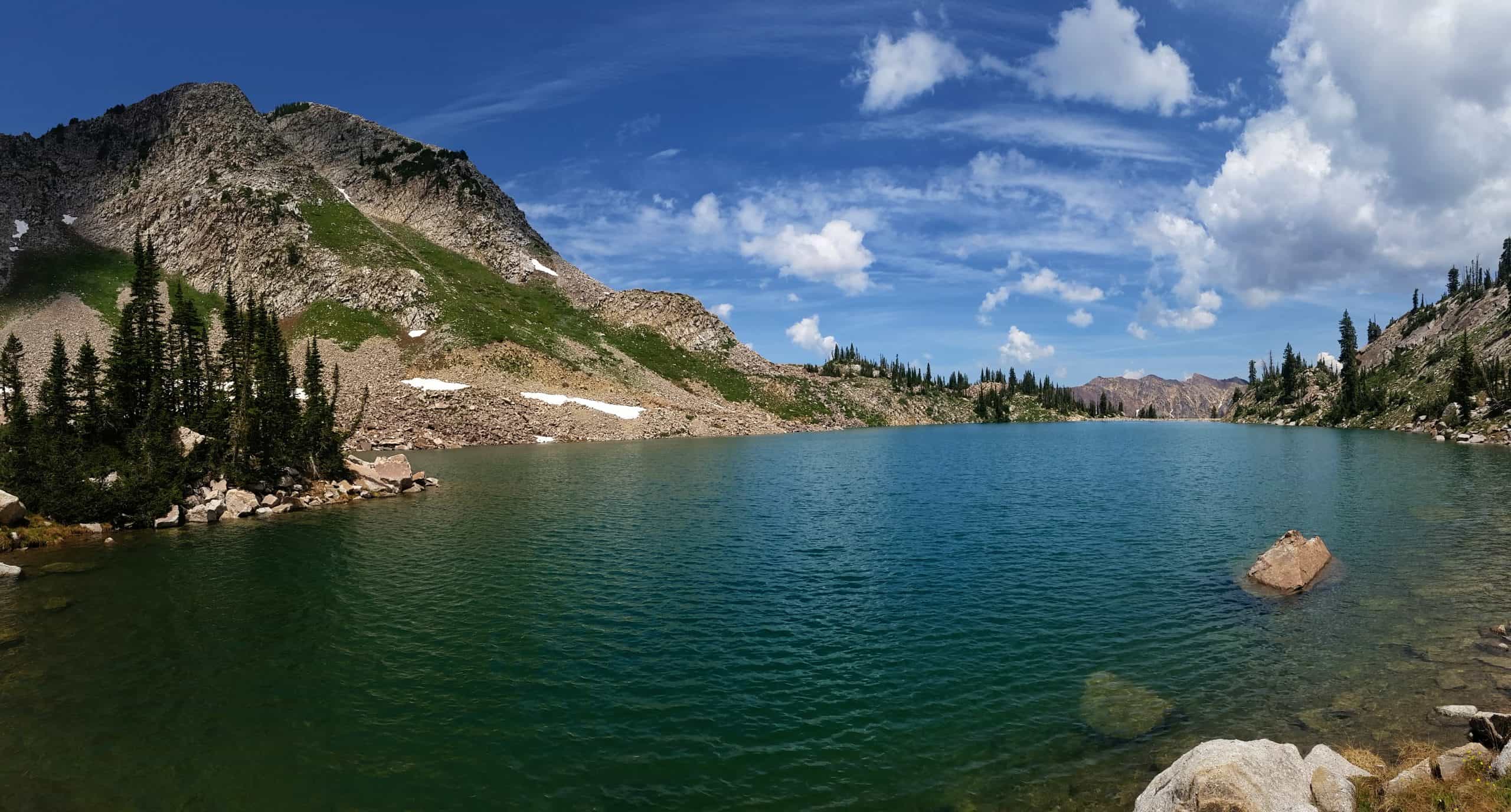 Wide shot of a blue alpine lake nestled among rugged mountain peaks on a clear day with scattered clouds.