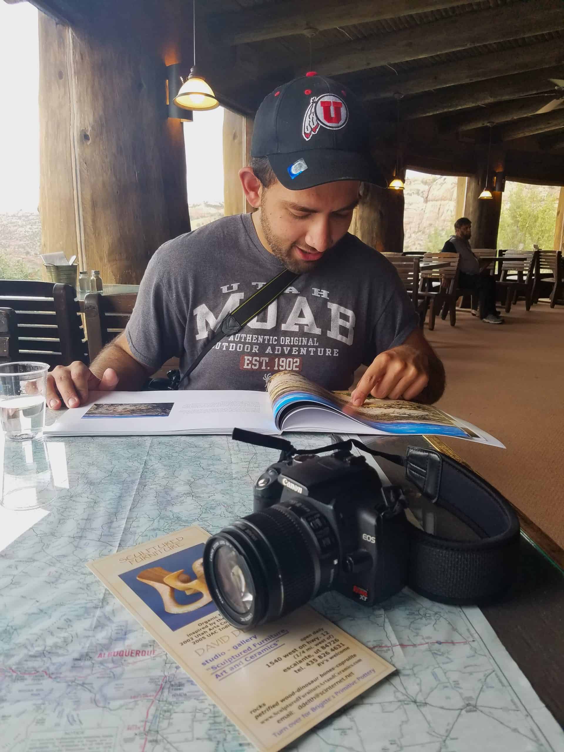 Man sitting at a table with a camera, map and travel book inside the cozy Kiva Koffehouse in Escalante, Utah
