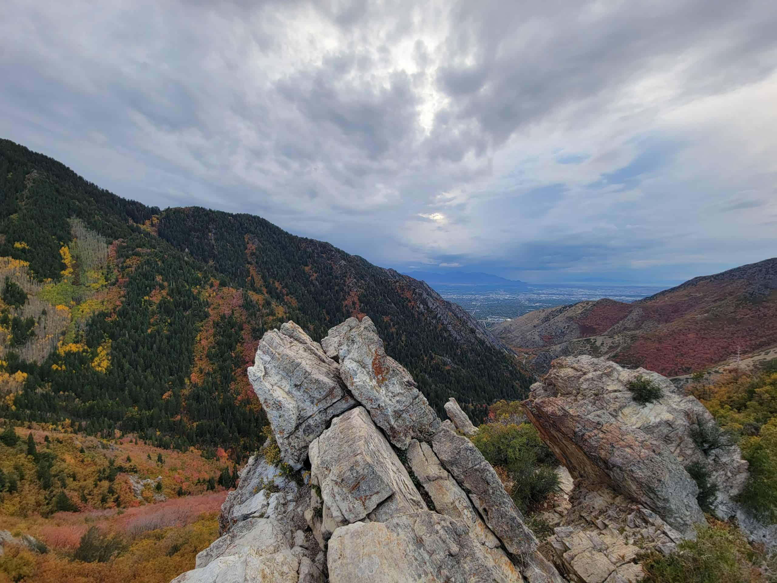 Rocky outcrop in the foreground contrasted with autumn views of Millcreek Canyon and Salt Lake City beneath moody skies.