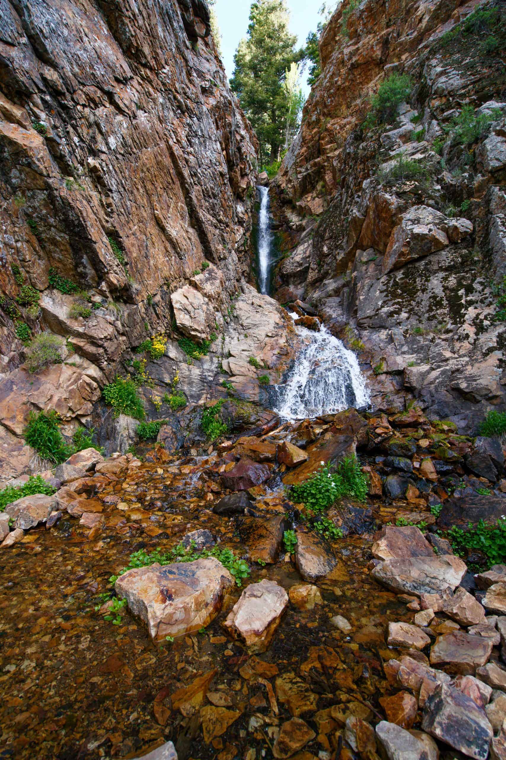 A rocky waterfall in Big Cottonwood Canyon, with two visible drops flowing into a shallow pool surrounded by rocky canyon walls, 