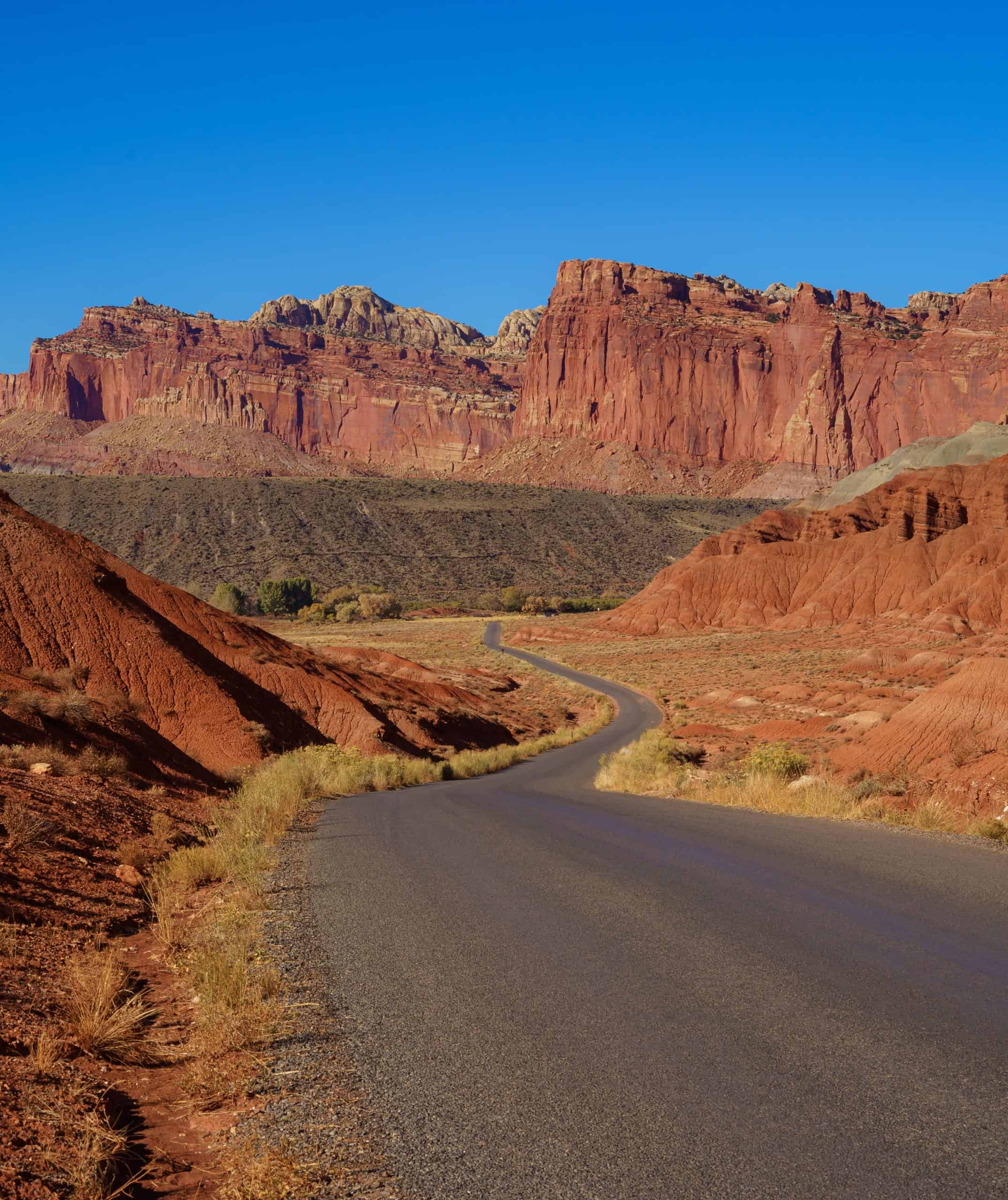 Scenic Road leading up to tall towering sandstone cliffs set against a blue sky in Capitol Reef National Park, Utah