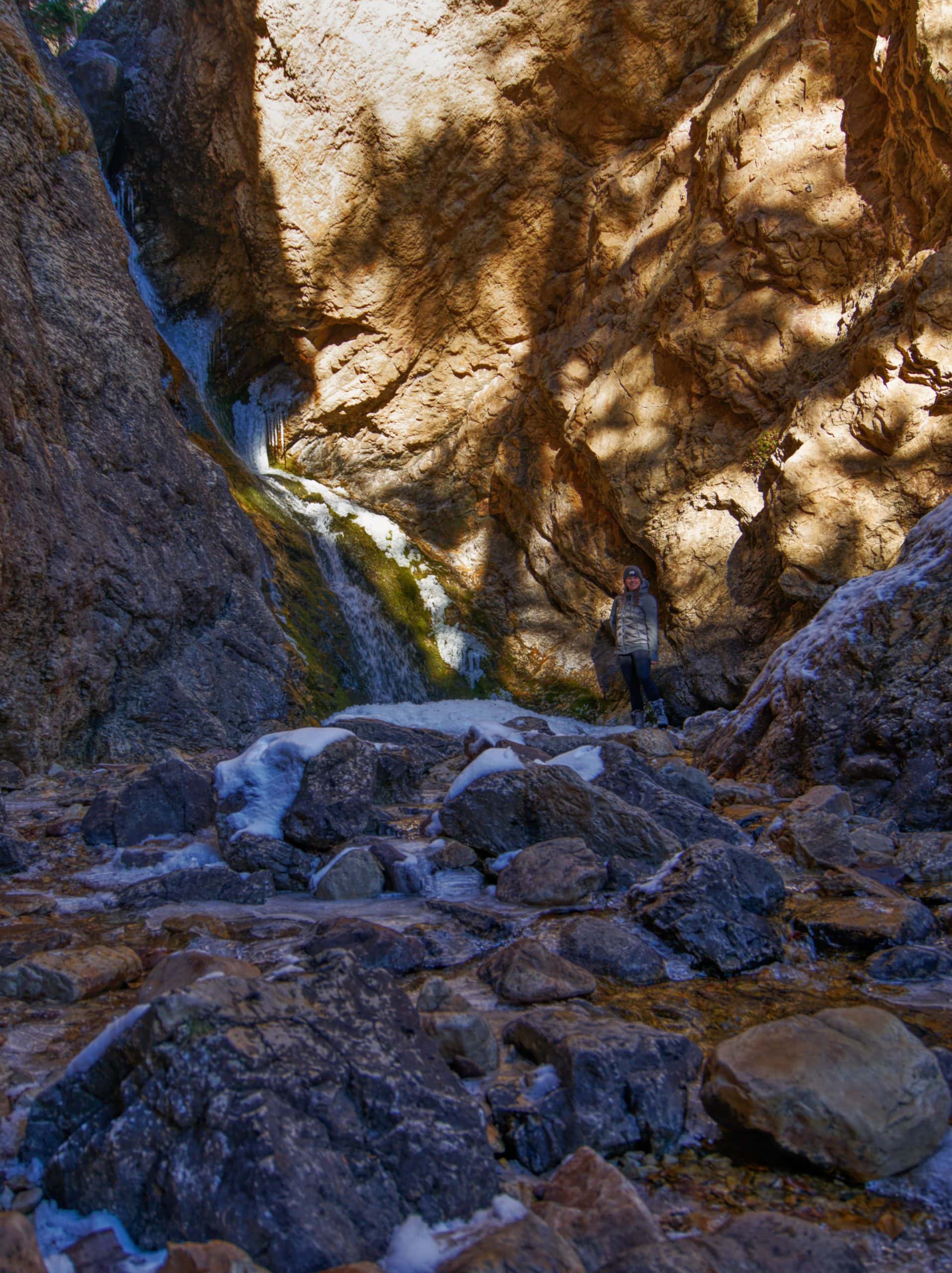 Hidden Falls cascading through a rocky canyon in Big Cottonwood Canyon with a hiker nearby for scale.