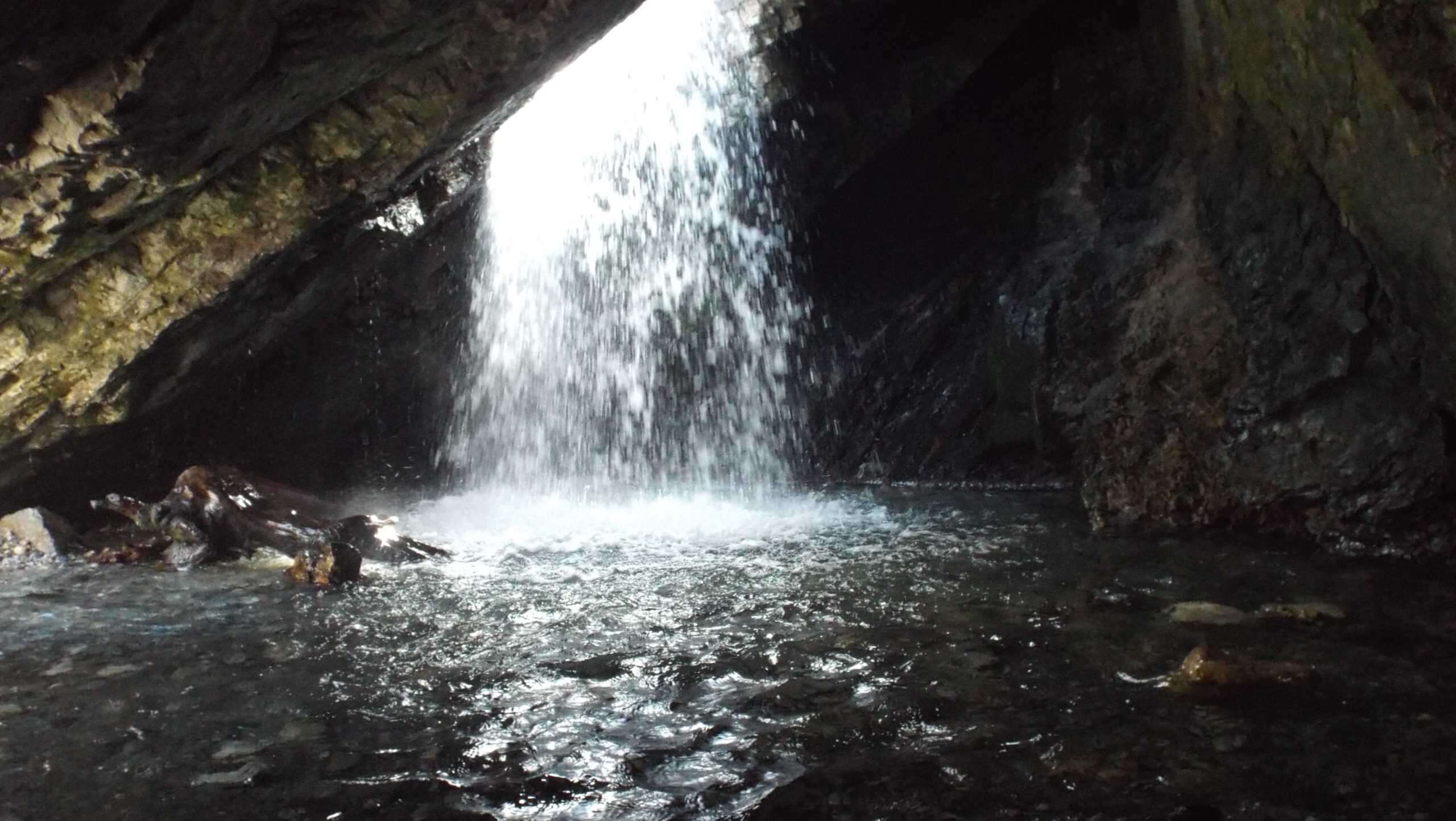 Waterfall pouring through the cave opening at Donut Falls in Big Cottonwood Canyon.