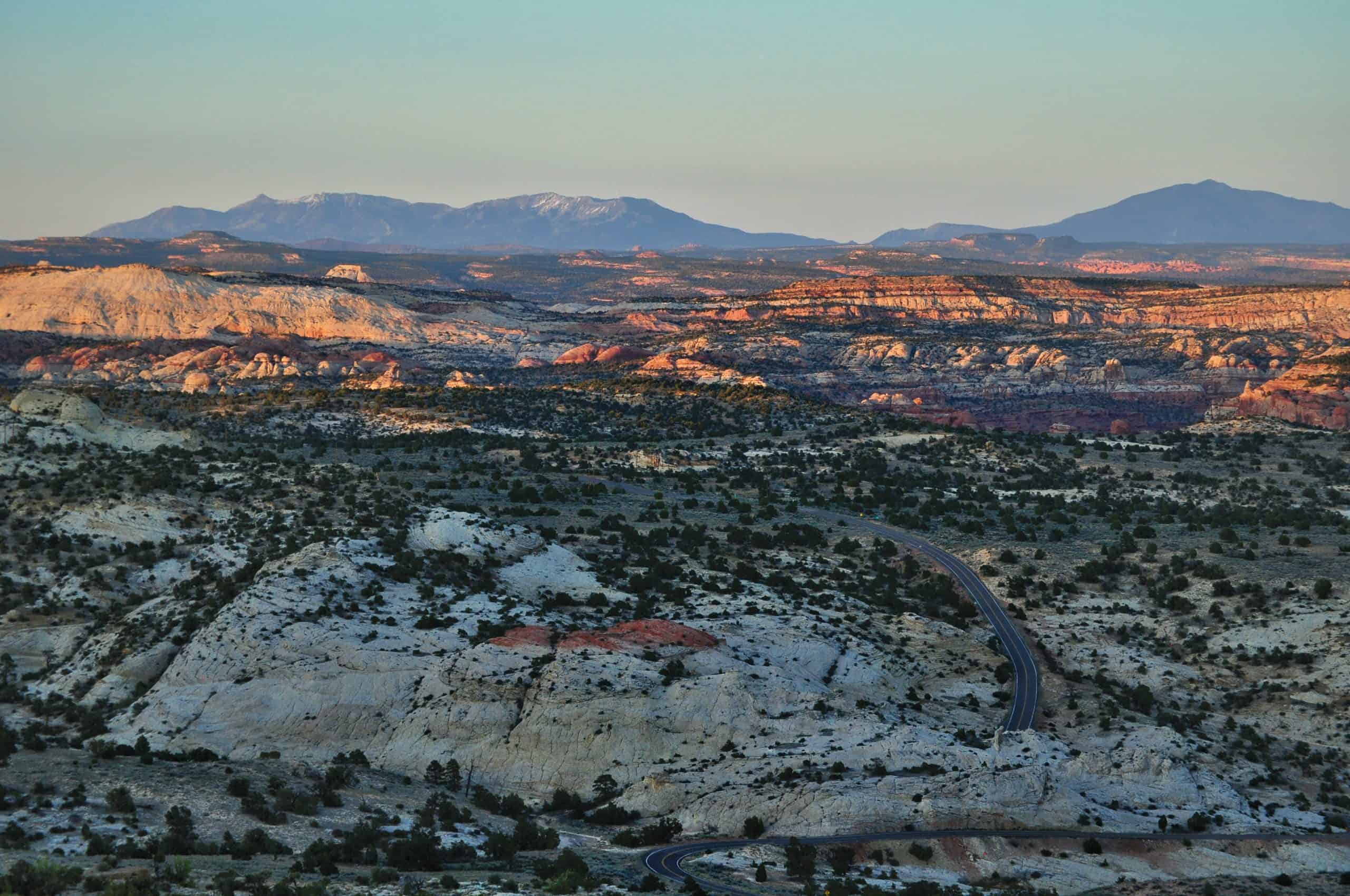 Wide open view of the Escalante region, with a road cutting through the vast colorful landscape at sunset. 