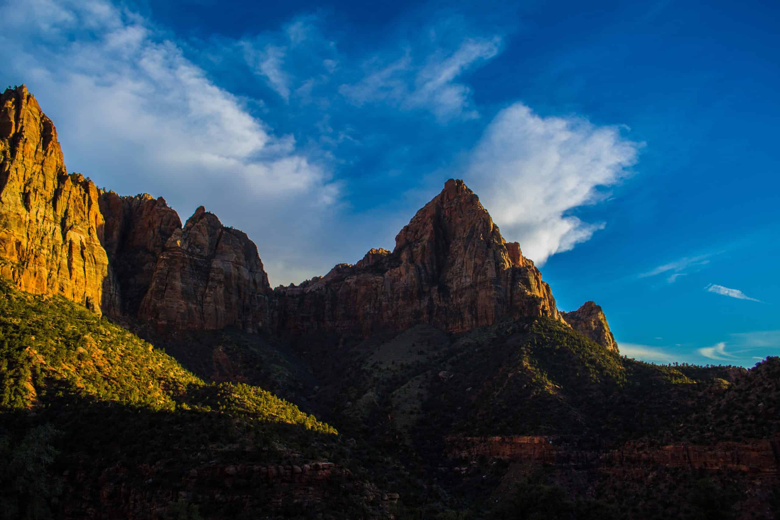 Sunset light on the Watchman rock formation in Zion National Park, Utah set against a partially blue sky. 