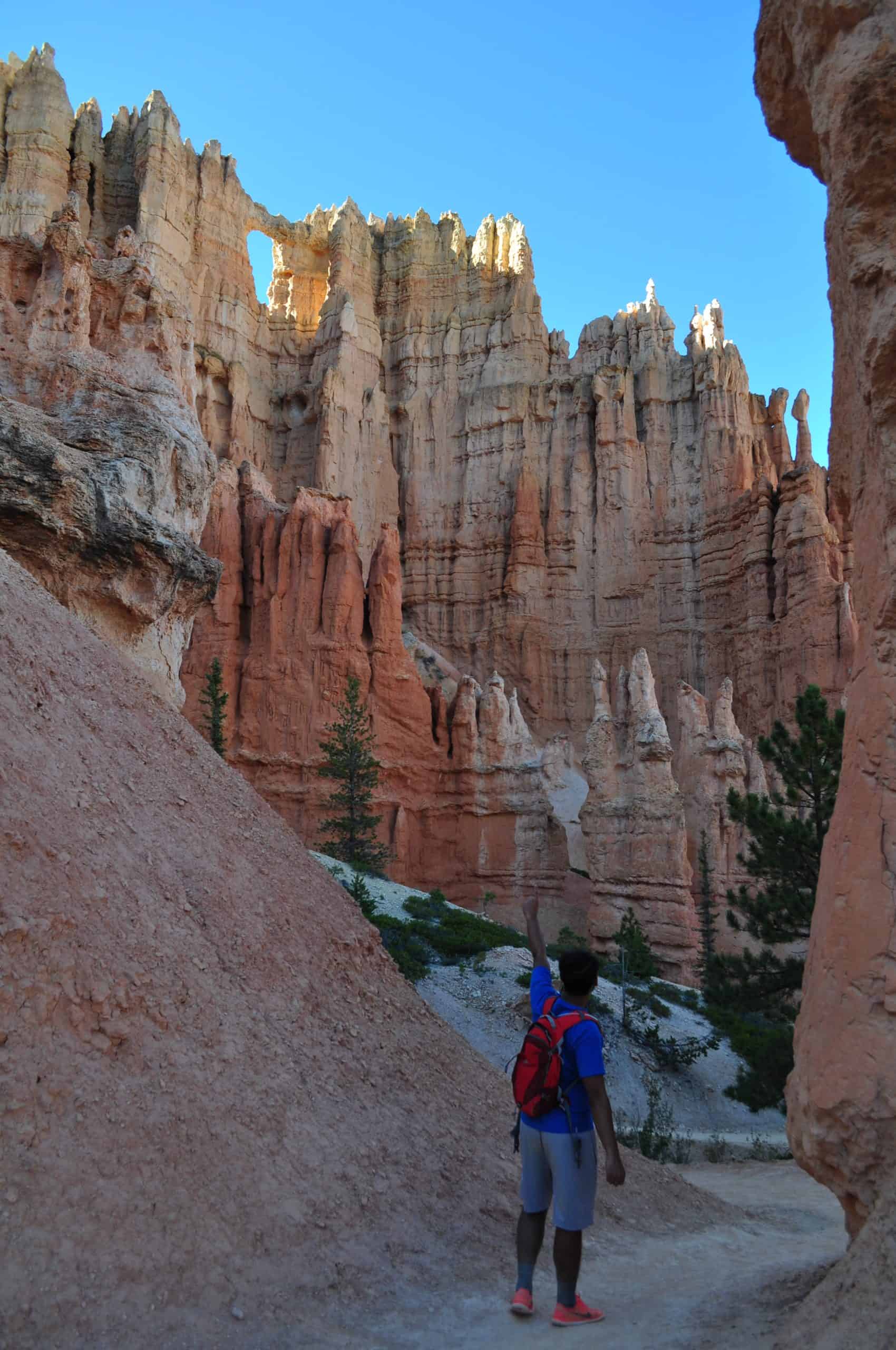 Man looks up towards a towering wall of hoodoos and a small arch at Bryce Canyon National Park, Utah.