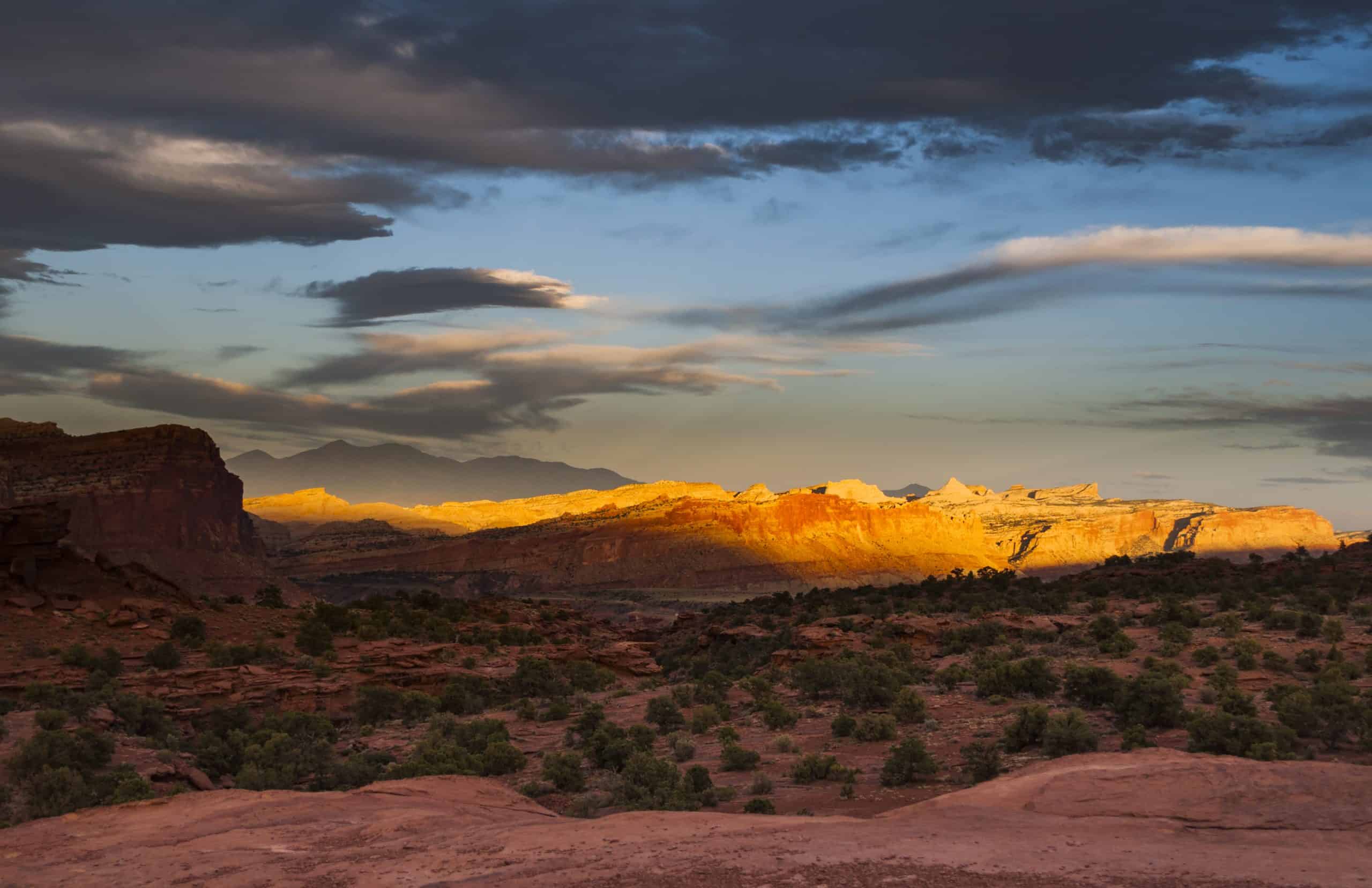 Sunset at Panorama Point in Capitol Reef National Park, Utah with golden light illuminating layered desert cliffs and distant mountains.