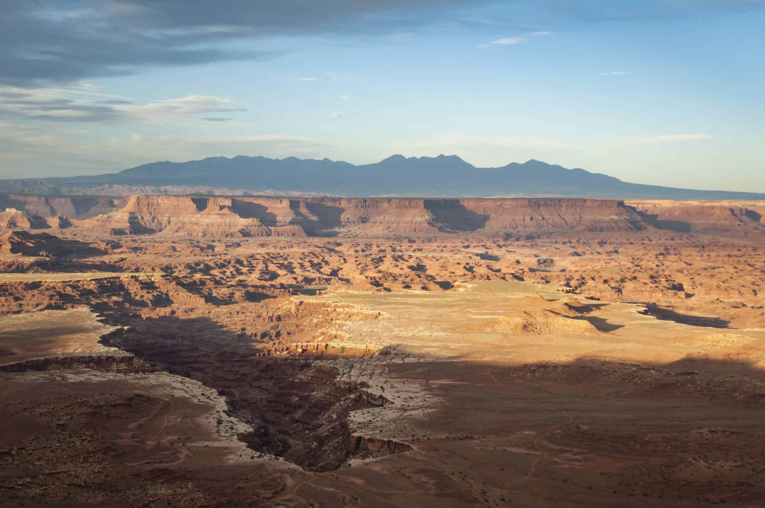 Vast expanse of Canyonlands National Park with the distant La Sal Mountains, with soft golden hour lighting. 