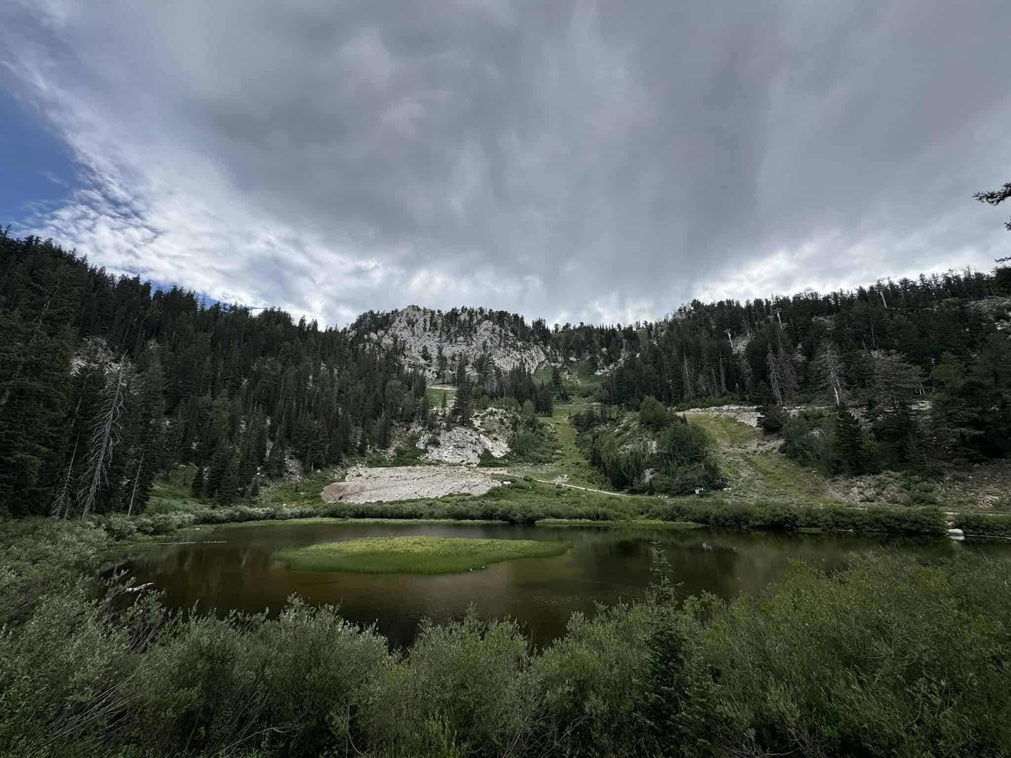 Moody clouds hanging over Lake Solitude with green shoreline and surrounding mountains.