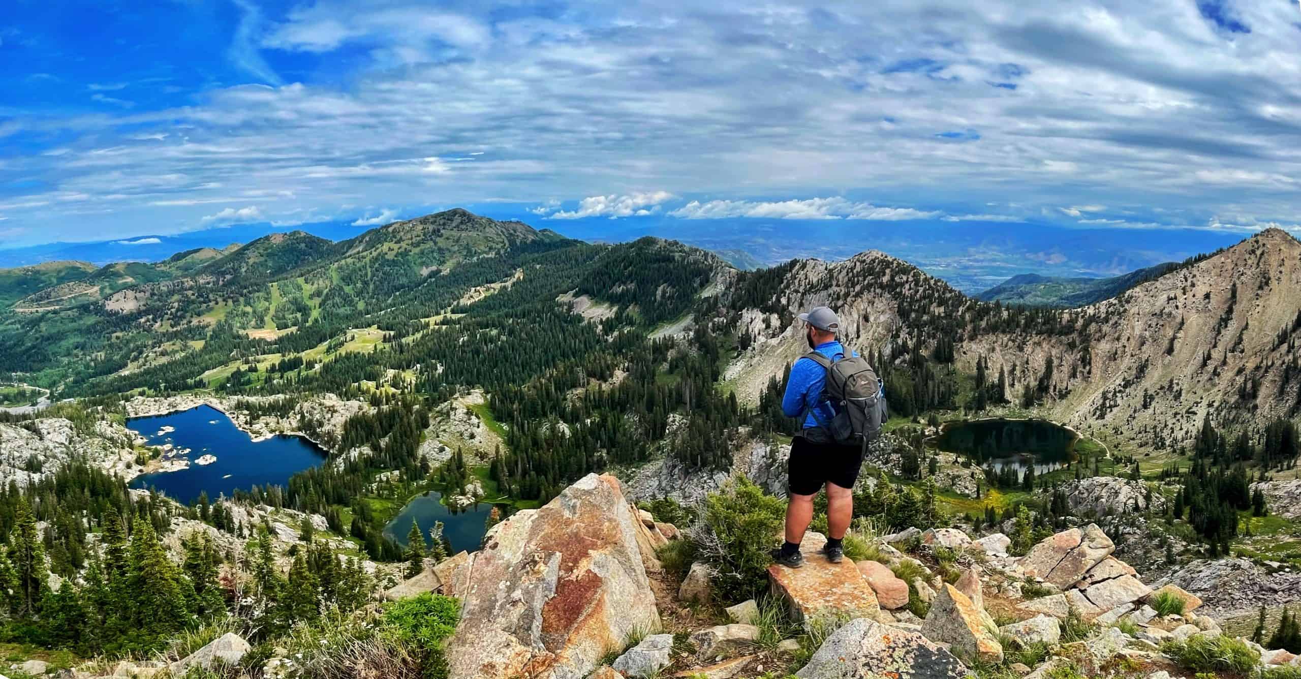 Hiker overlook beautiful panoramic view of distant mountains, green slopes and three alpine lakes in Big Cottonwood Canyon