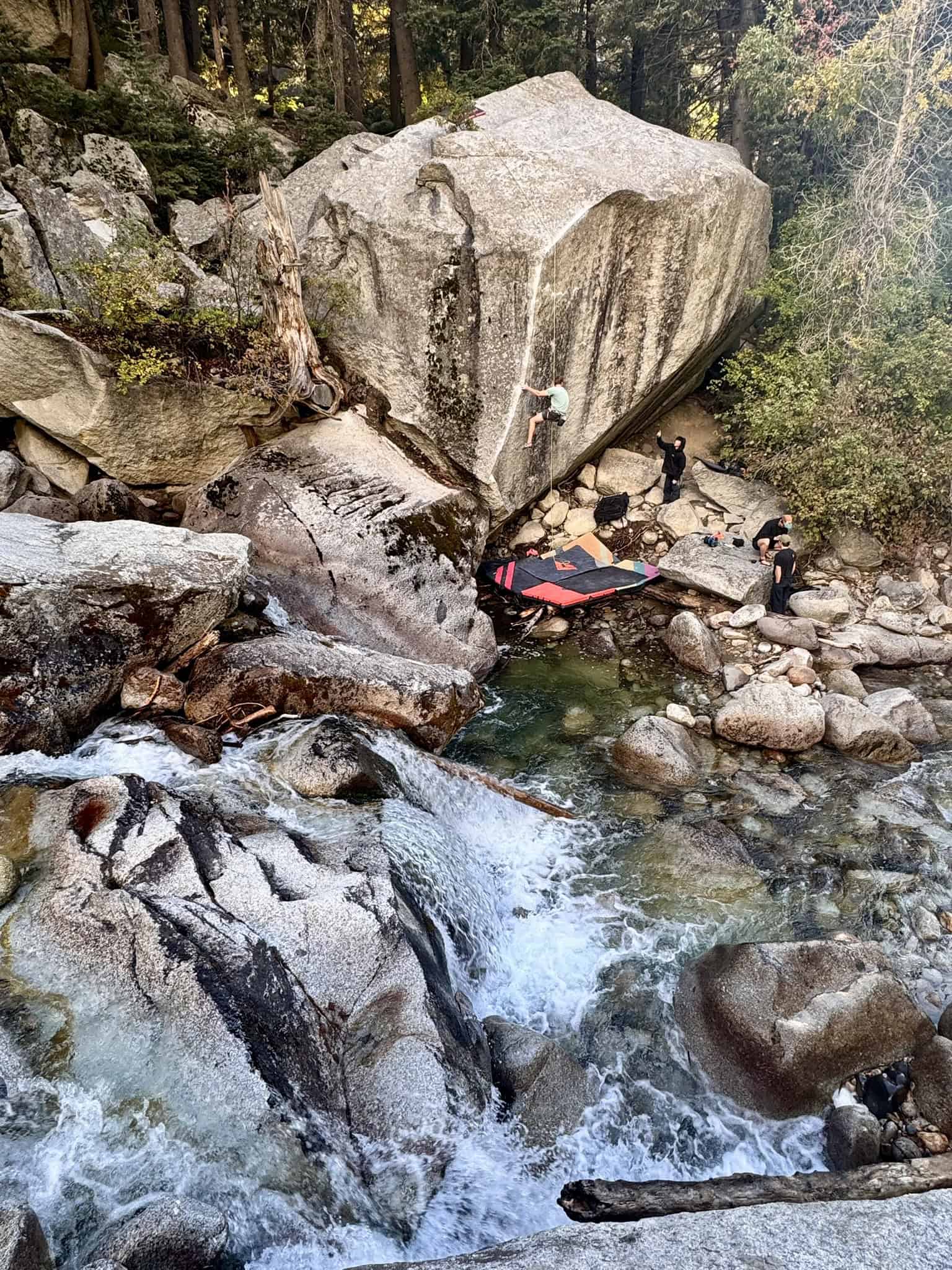 Rock climbers and crash pads beside a small waterfall and granite boulders along a creek in Little Cottonwood Canyon.