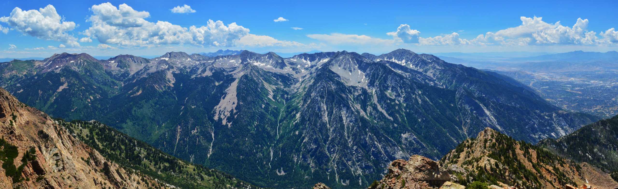 Wide panoramic view from the summit of Broads Fork Twin Peaks overlook a deep canyon, rugged mountain peak and open skies