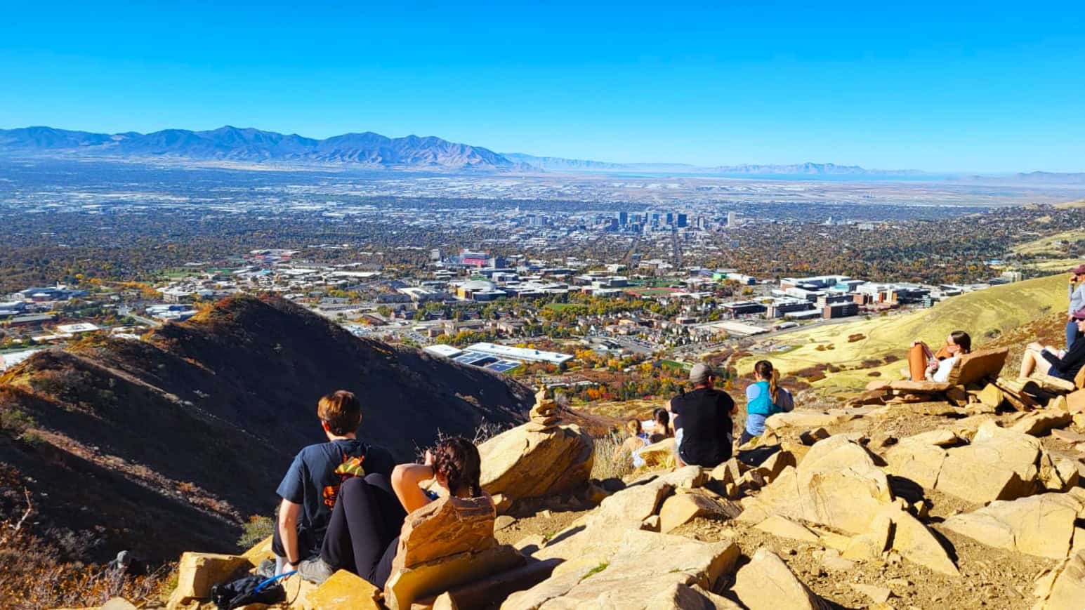 Scenic view of the Salt Lake Valley from an overlook with people sitting on rocks shaped like living room chairs