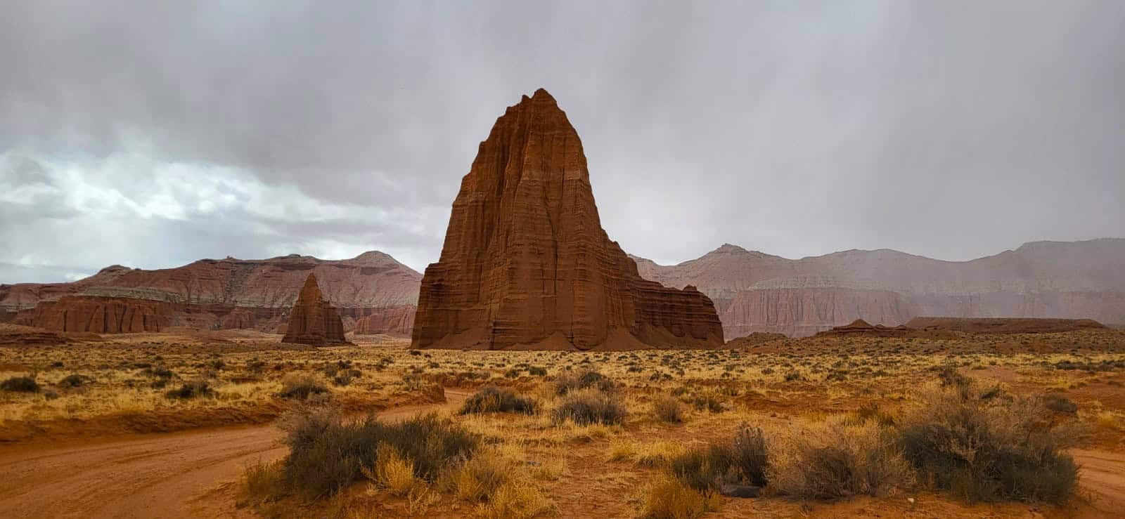 Temple of the Sun rising from Cathedral Valley with dramatic rock formations, open desert and rain off in the distance. 