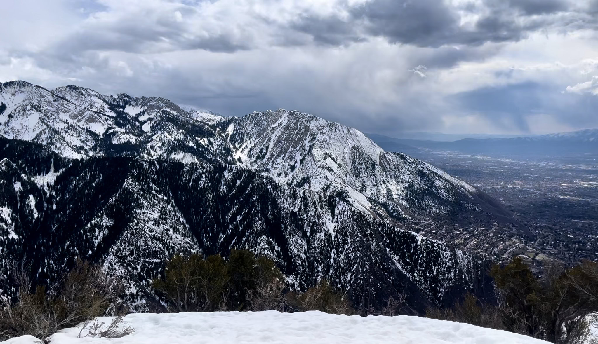 Panoramic view from the summit of Grandeur Peak in winter, with snowcapped mountains in the background.