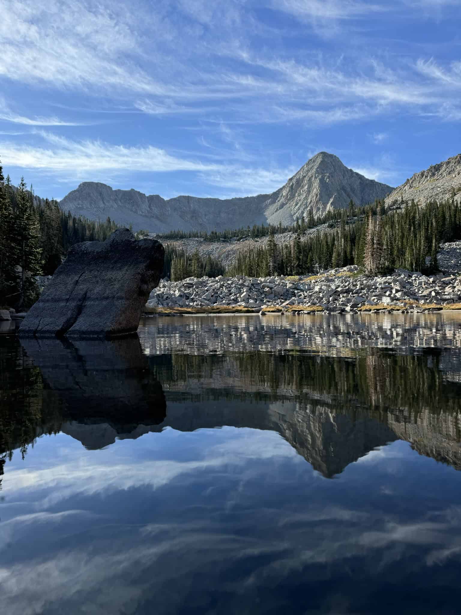 A serene view of Lower Maybird Lake, with its calm waters reflecting Pfeifferhorn and large granite boulders