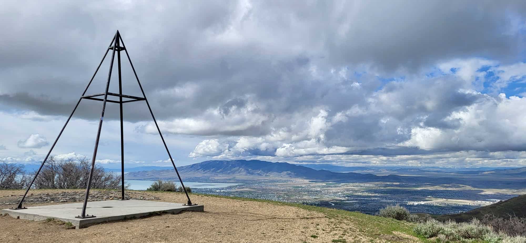 Metal structure known as the alien tower sits on top of a mountain with distant lake, mountains and city views. 