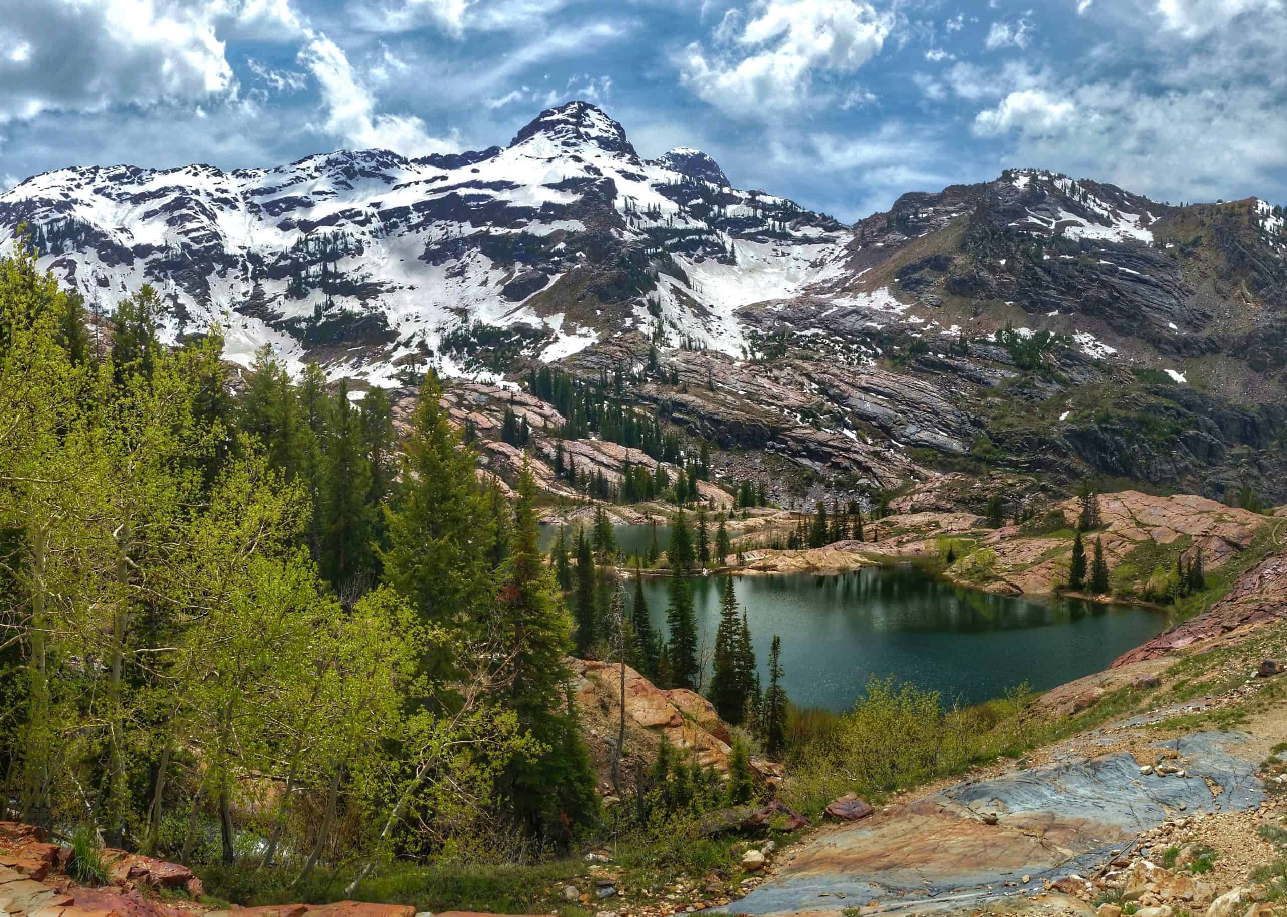 A scenic alpine view of Lake Florence in the foreground with Lake Lillian behind it, nestled among rugged peaks and green trees under a cloudy sky.

