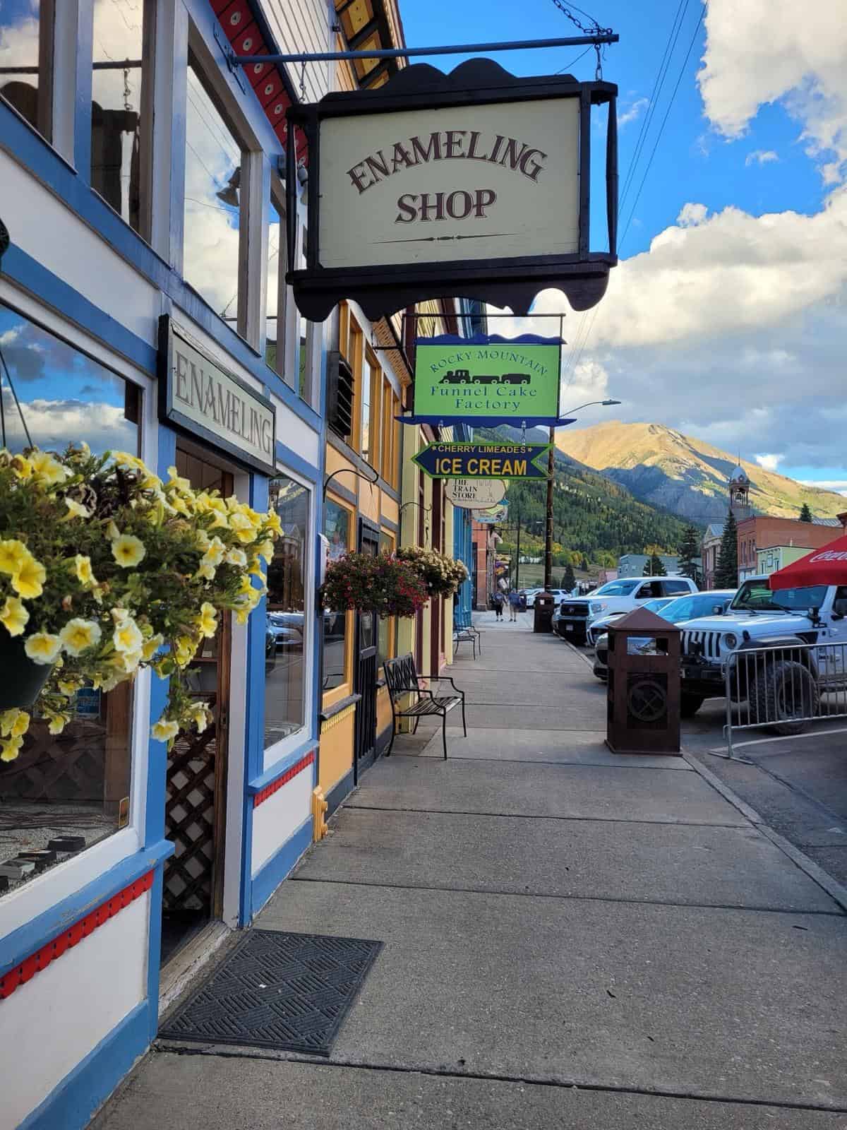 A sunny street scene on Silverton Main Street, featuring vibrant buildings, hanging flower baskets, and mountain views, capturing the charming atmosphere of the historic town