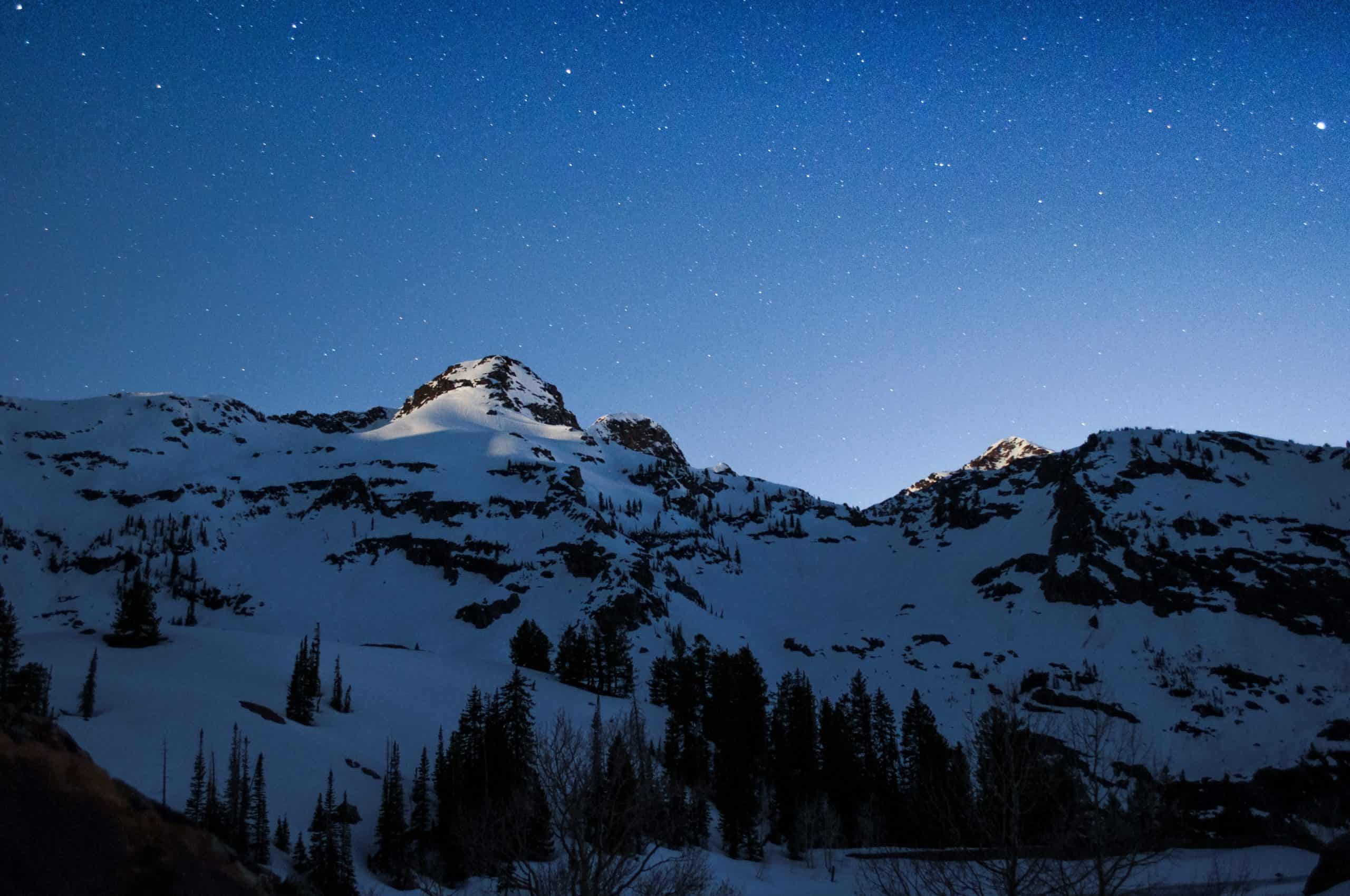A serene scene of moonlit snowy mountain peaks, viewed from Lake Blanche under a starry night sky.