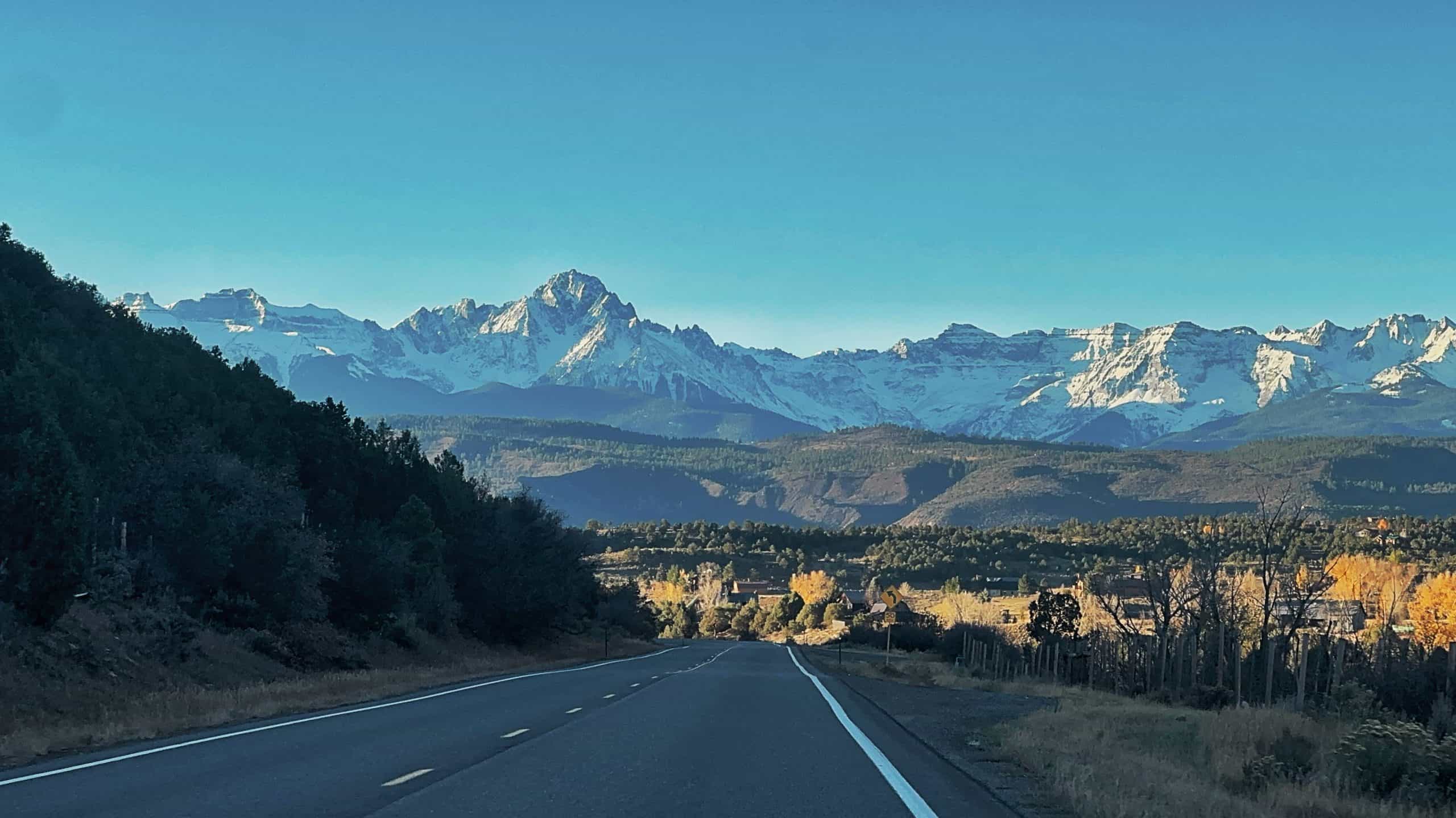 A scenic road leading to a dramatic view of snow capped peaks under blue skies near Ridgeway, Colorado. 