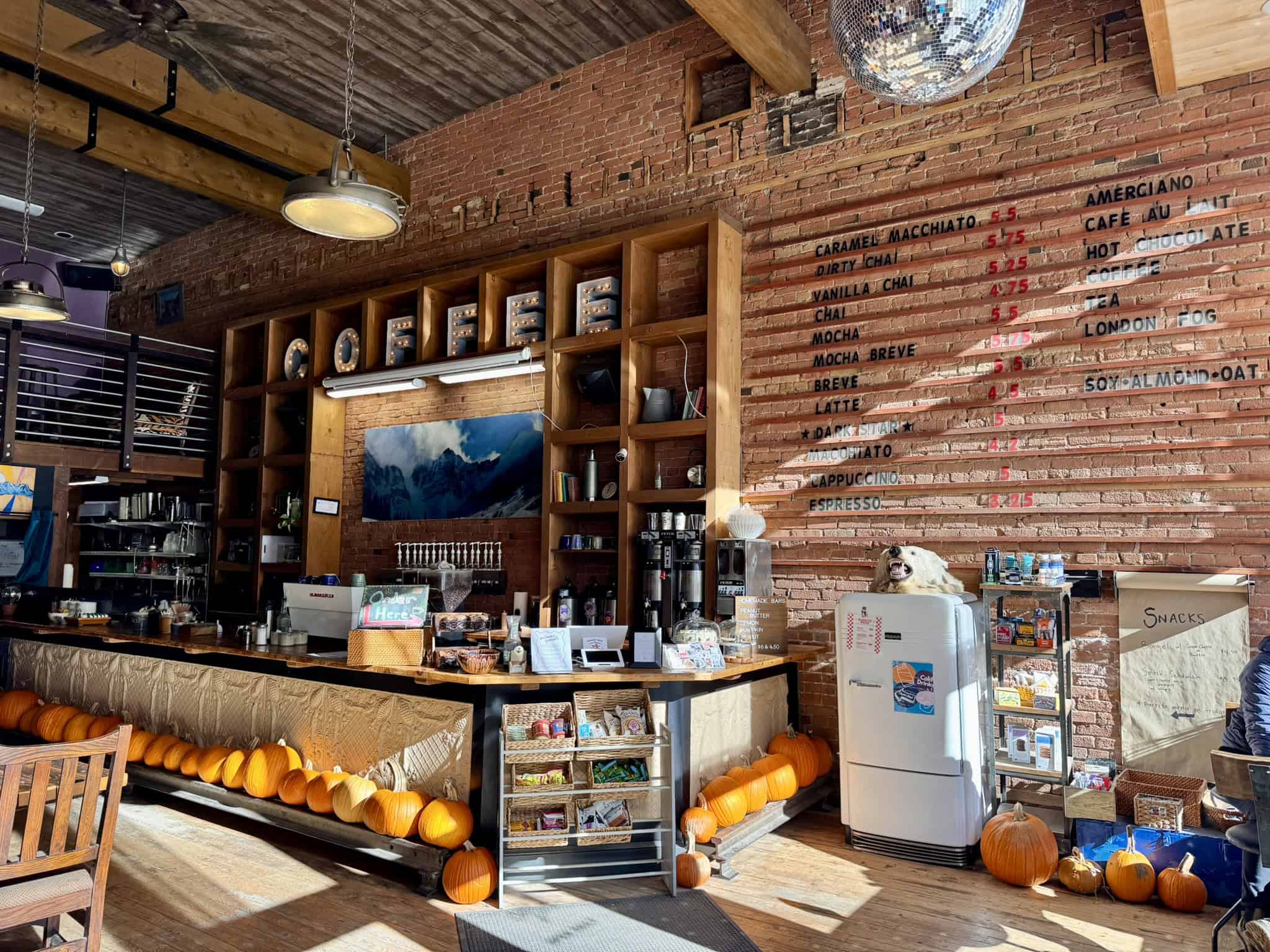 The cozy interior of Coffee Bear, featuring exposed brick walls, wooden shelves, warm lighting, and autumn pumpkins, offering a welcoming spot in Silverton, Colorado. 