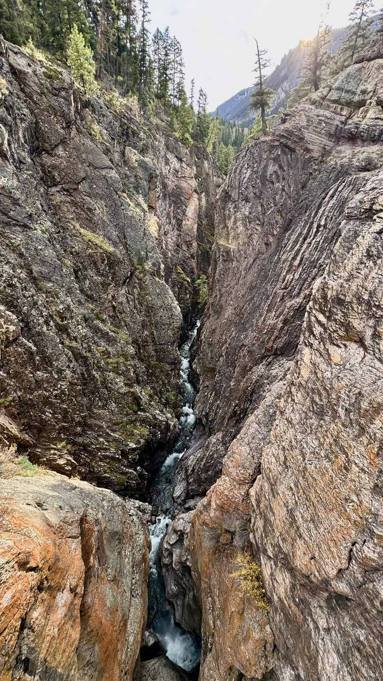 A narrow, rugged canyon with steep rocky walls and a cascading stream below, viewed from the High Bridge Trail, one of the best things to do in Ouray

