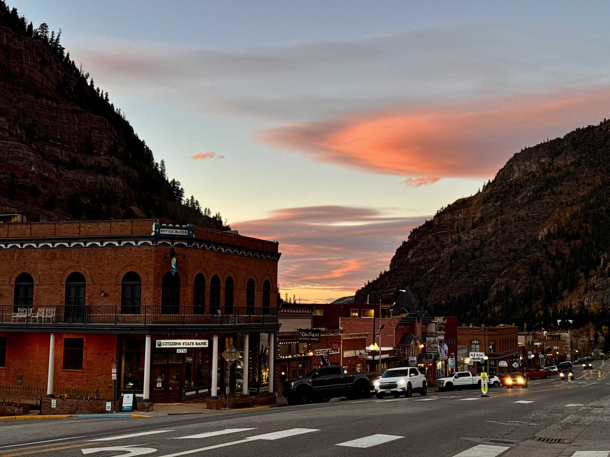 A scenic view of downtown Ouray at sunset, with colorful skies over historic buildings and towering canyon walls,