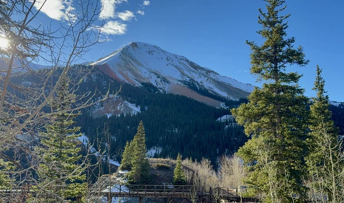 A scenic view of Red Mountain from the Red Mountain Overlook, featuring a snow-dusted peak rising above evergreen trees under a clear blue sky