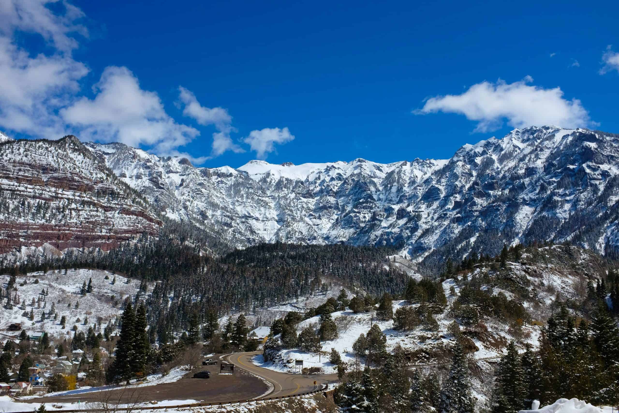A snowy mountain landscape with a winding road through pine trees and rugged peaks, showcasing winter hiking as one of top best things to do in Ouray.