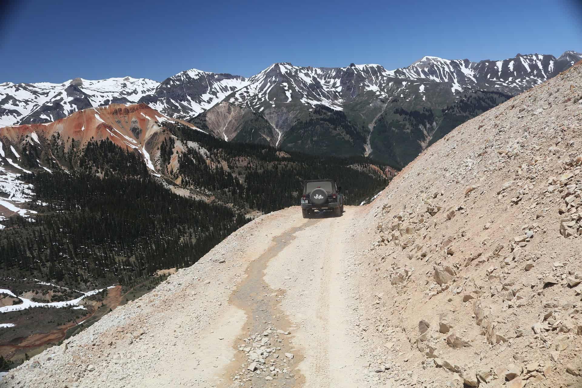 A jeep driving along a dirt road near Ouray, with a stunning panorama  of snow-capped peaks and colorful ridges in the under a blue sky