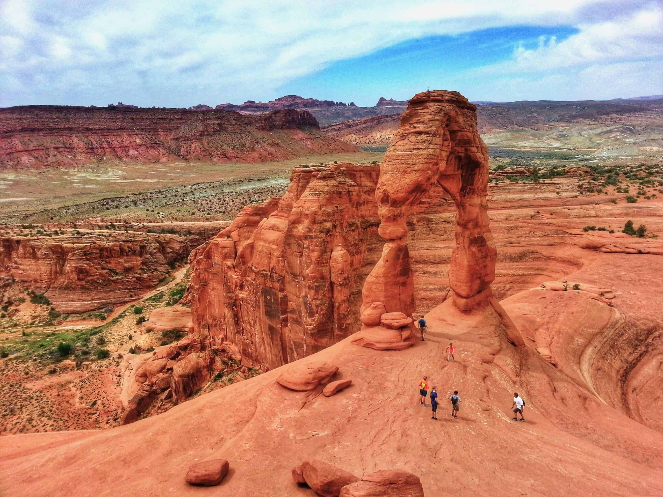 The breathtakingly unique Delicate Arch,  one of most iconic hikes in Utah, viewed from above, set against a stunning backdrop of red rocks