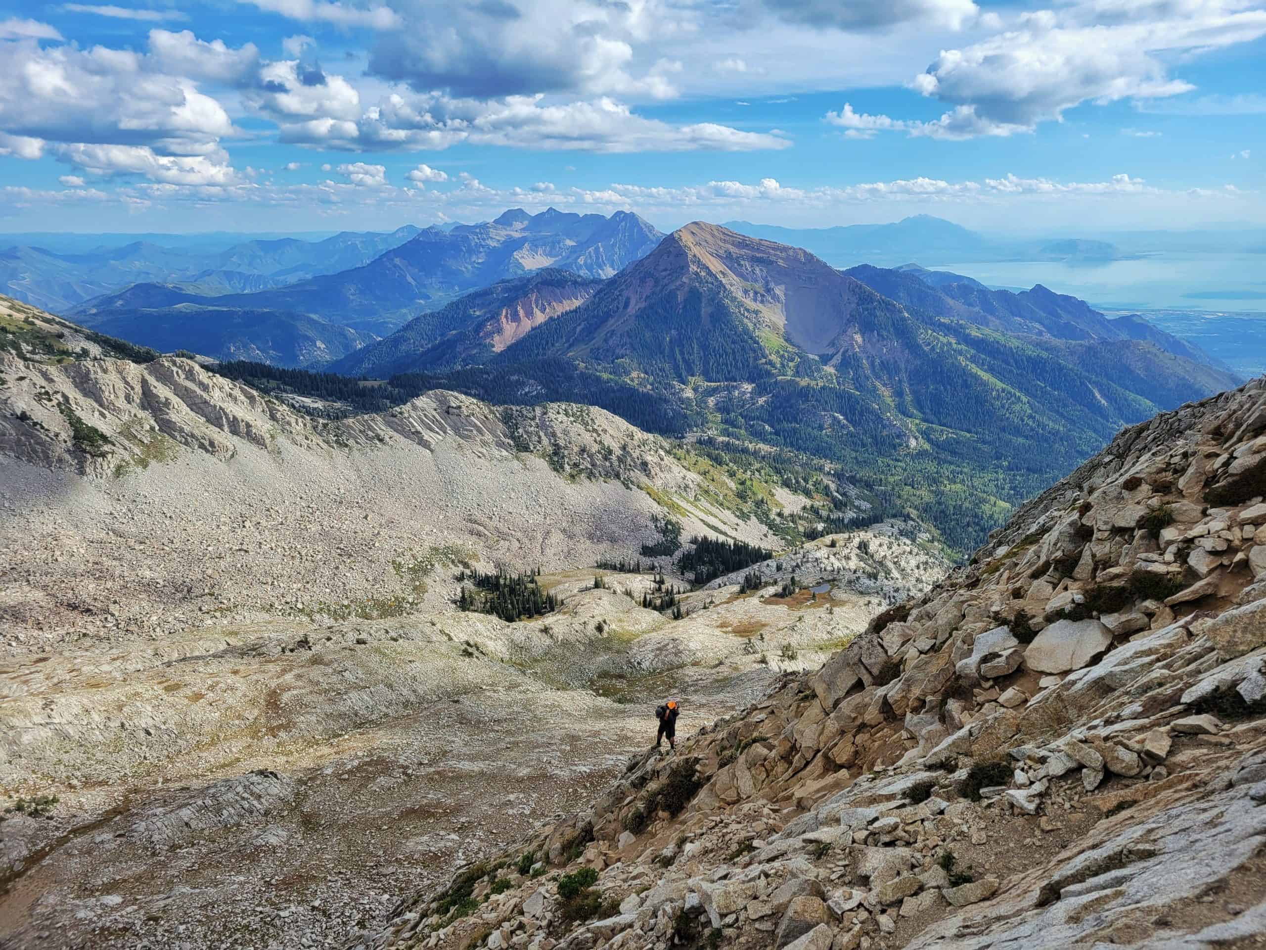 A hiker descends a steep, rocky slope from Pfeifferhorn, with vast mountain ridges stretching across the horizon, on one of the best hikes in Utah.

