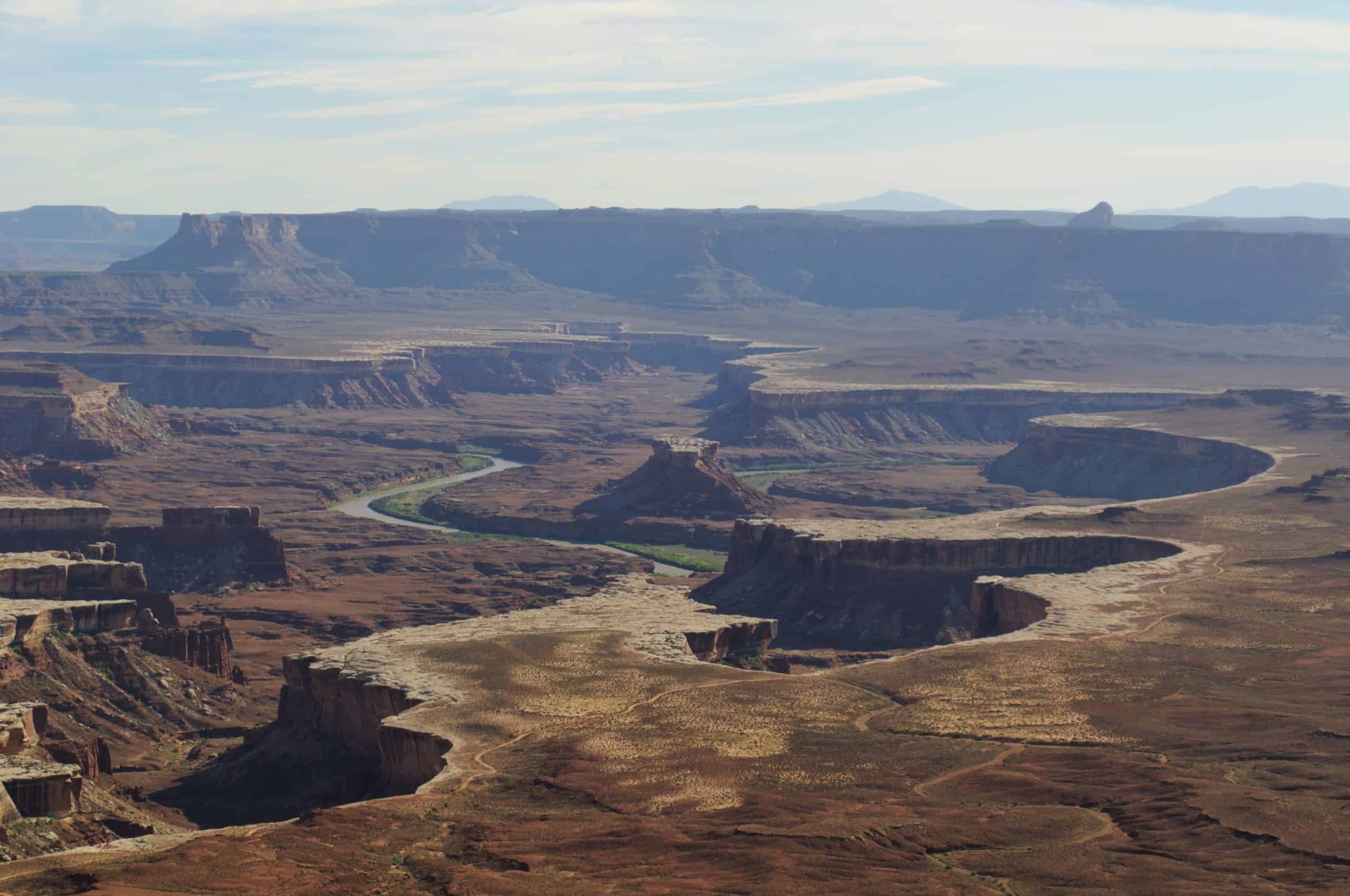 A vast view captures the winding Green River carving through layered red rock mesas and vast canyon floors in Canyonlands National Park
