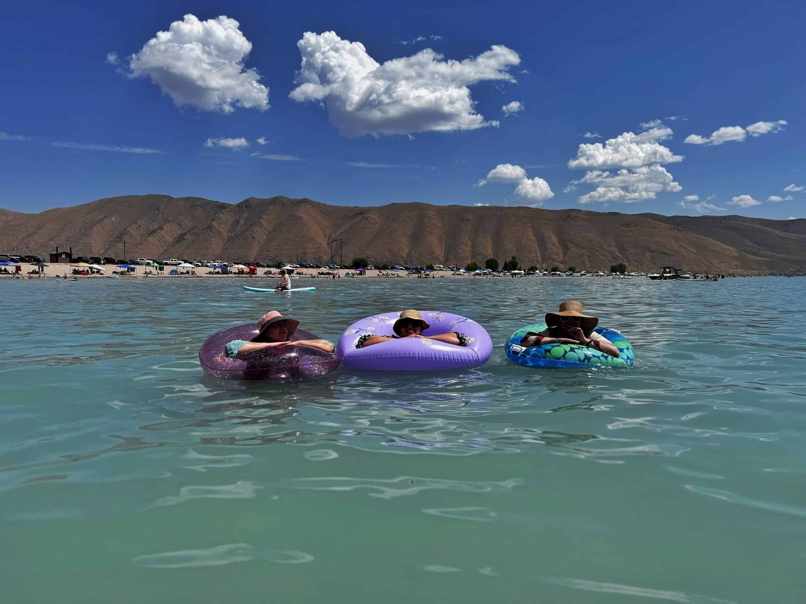 Three people relaxing in inflatable tubes  in Bear Lake's emerald waters, with distant hills under a bright blue sky