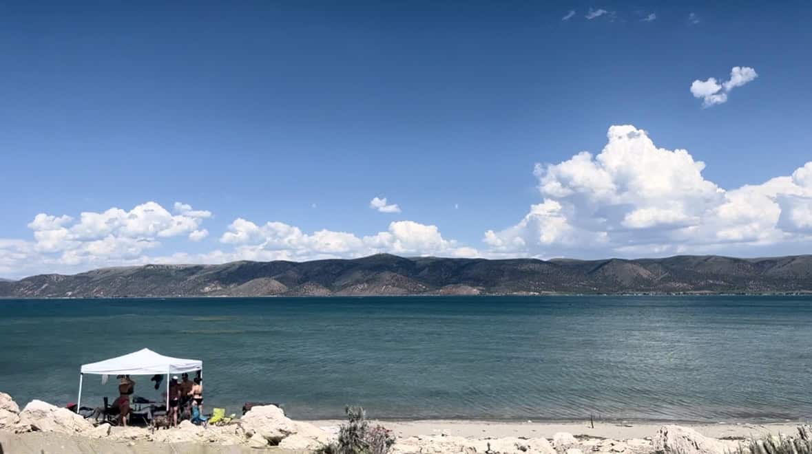 A stunning view of Bear Lake's emerald green color, set against distant mountain peaks, clouds and blue skies. 