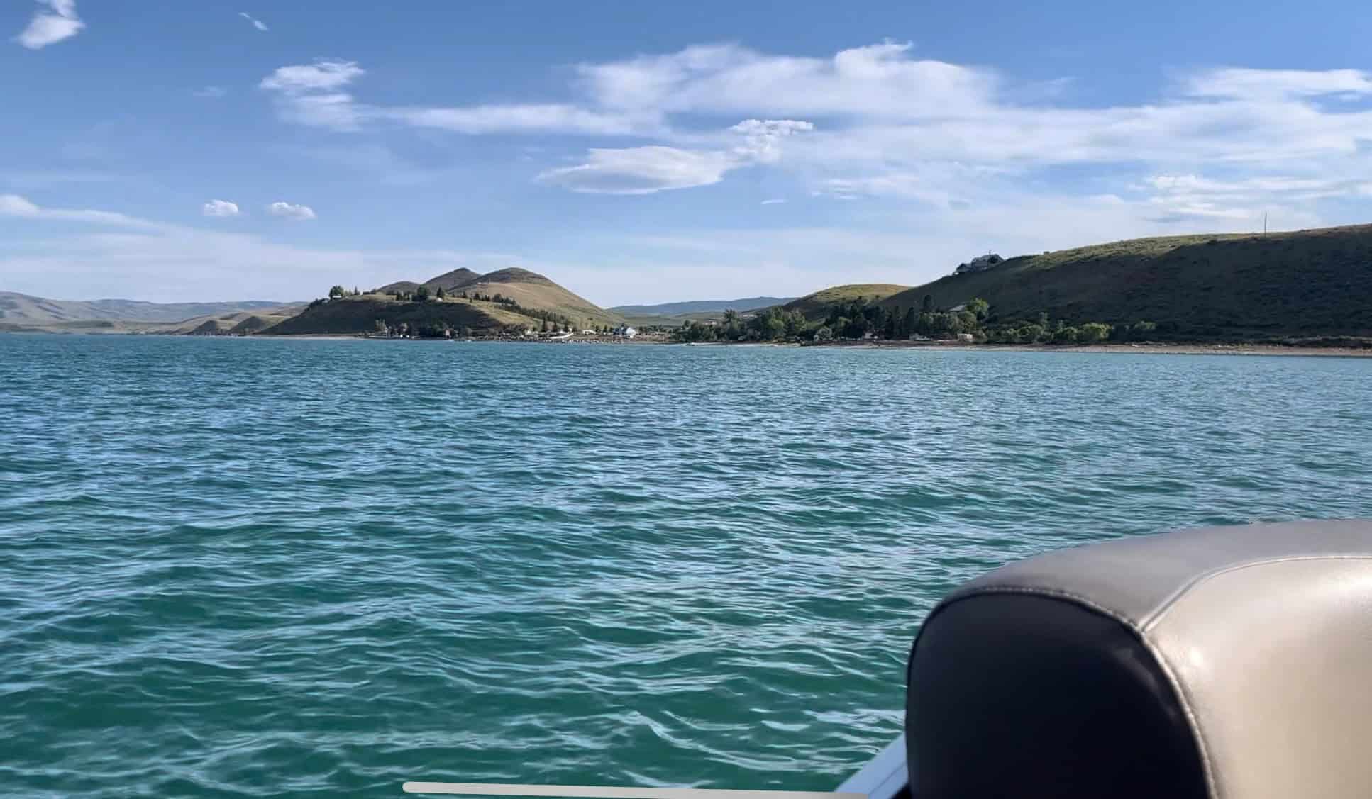 Open water view from a boat on Bear Lake, with glassy emerald water and distant hills and scattered trees. 