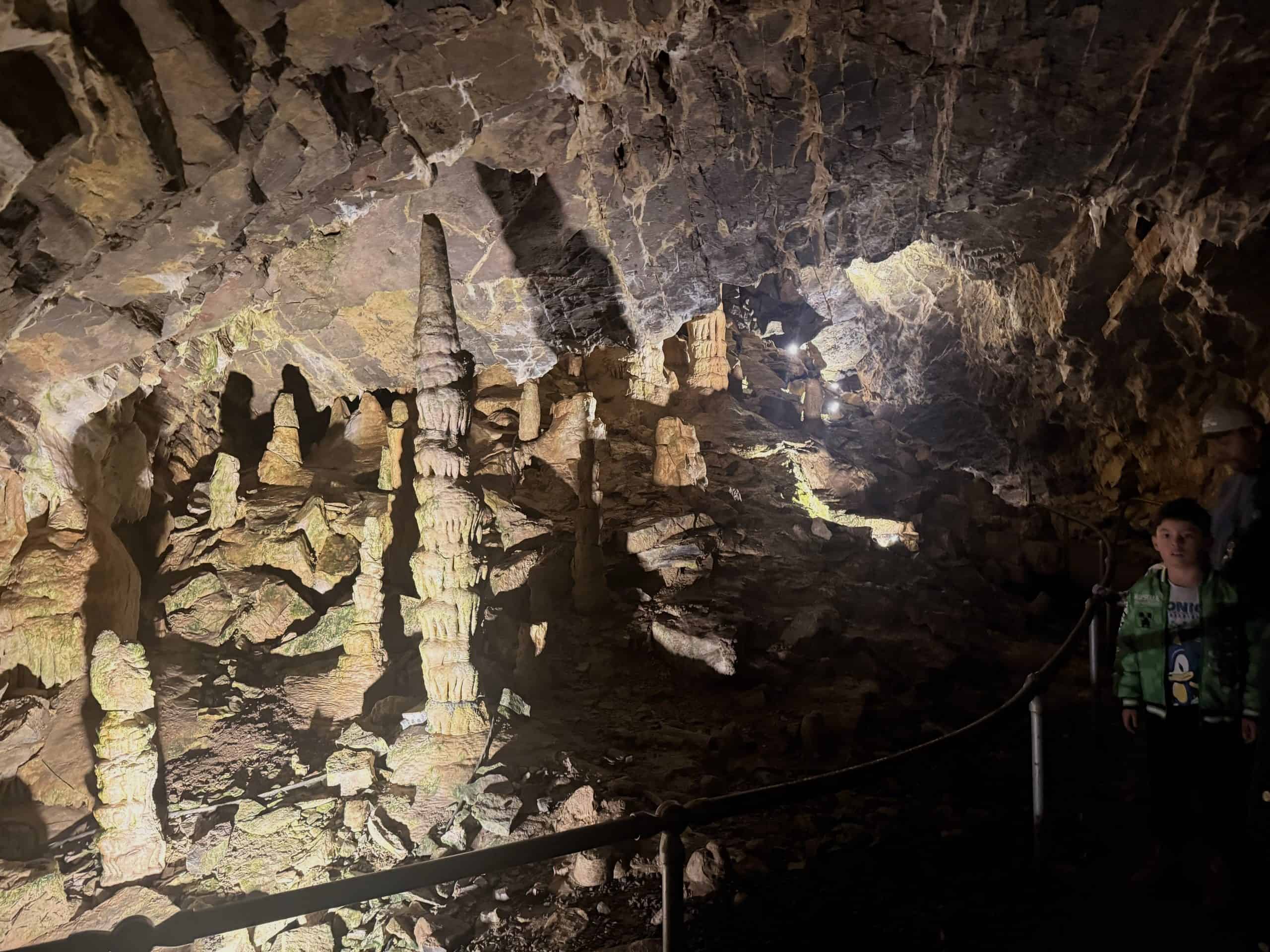 Illuminated rock formations and towering stone pillars rise from the cavern floor behind a safety railing, revealing the stunning natural geology inside Minnetonka Cave.