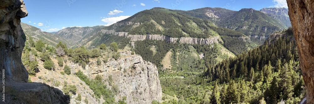 A panoramic view from a rocky overhang looking out over steep, forested slopes and distant mountain ridges, showcasing the dramatic scenery found on hikes near Bear Lake.