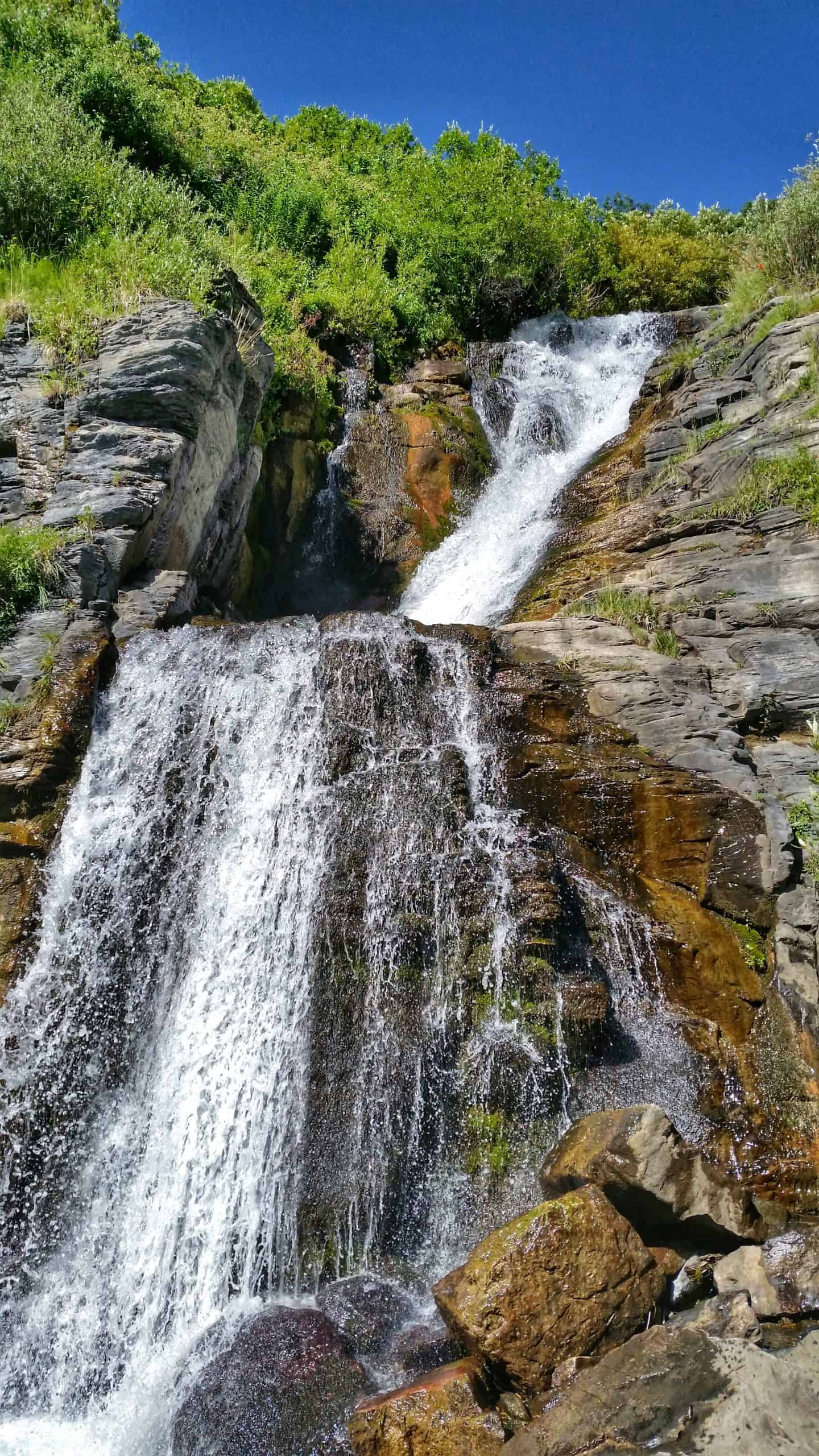 The First Falls on the Mountain Timpanogos Hike, cascading over distinct rocky tiers, with vibrant green vegetation lining the banks