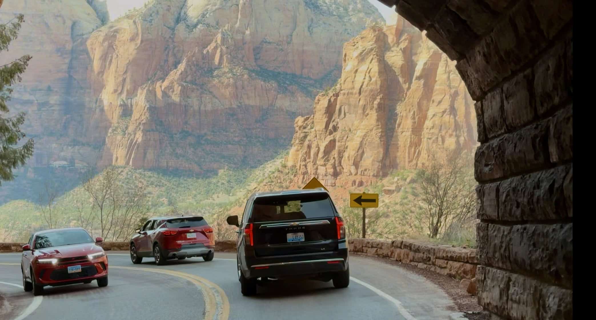 Cars driving out of a brick-lined tunnel with a stunning sight of Zion Canyon in the distance illuminated in bright sunshine. 